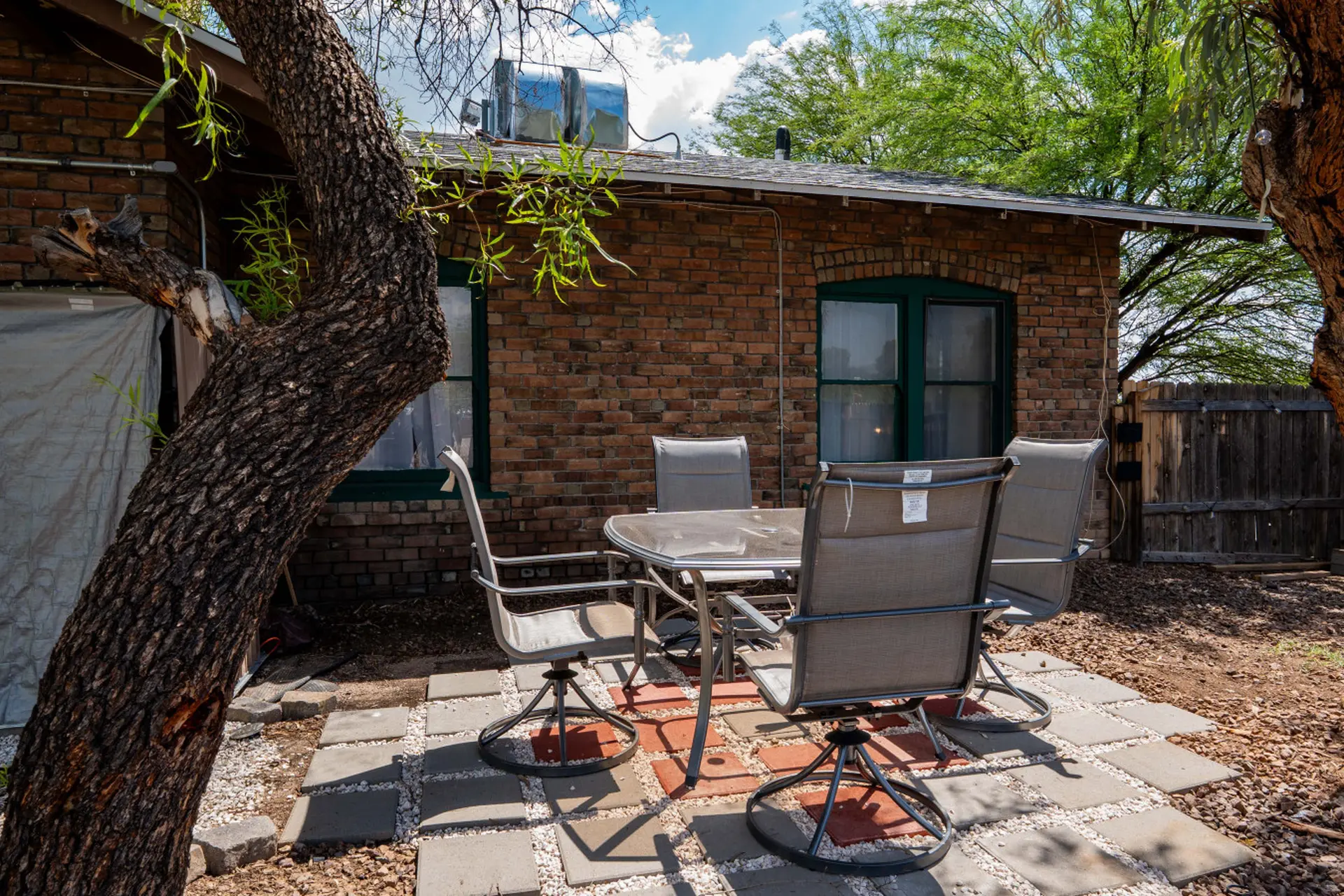 A patio table and chairs are on a stone patio in front of a brick building.