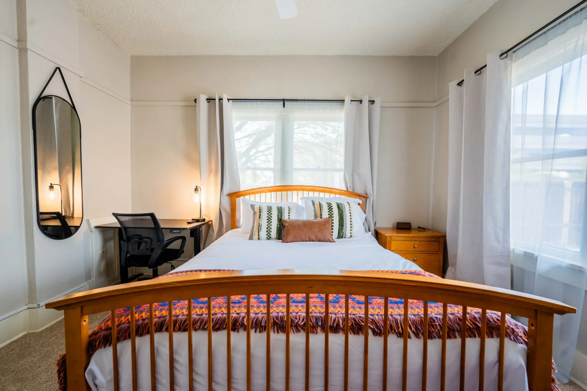 A bedroom with a wooden bed, a desk, and a mirror.