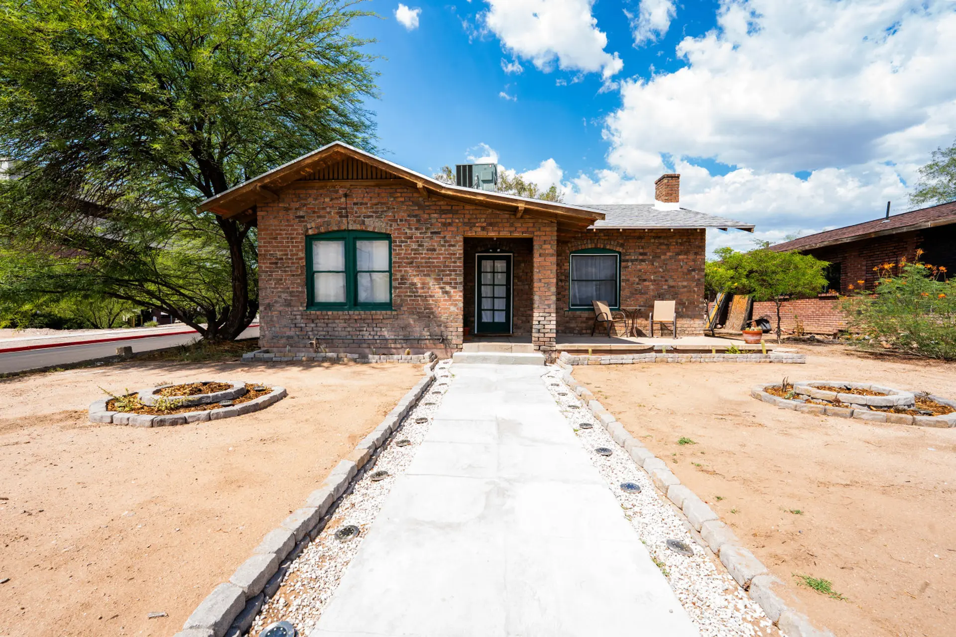 Front view of a single-story brick house with green trim, a covered porch, and a concrete walkway.