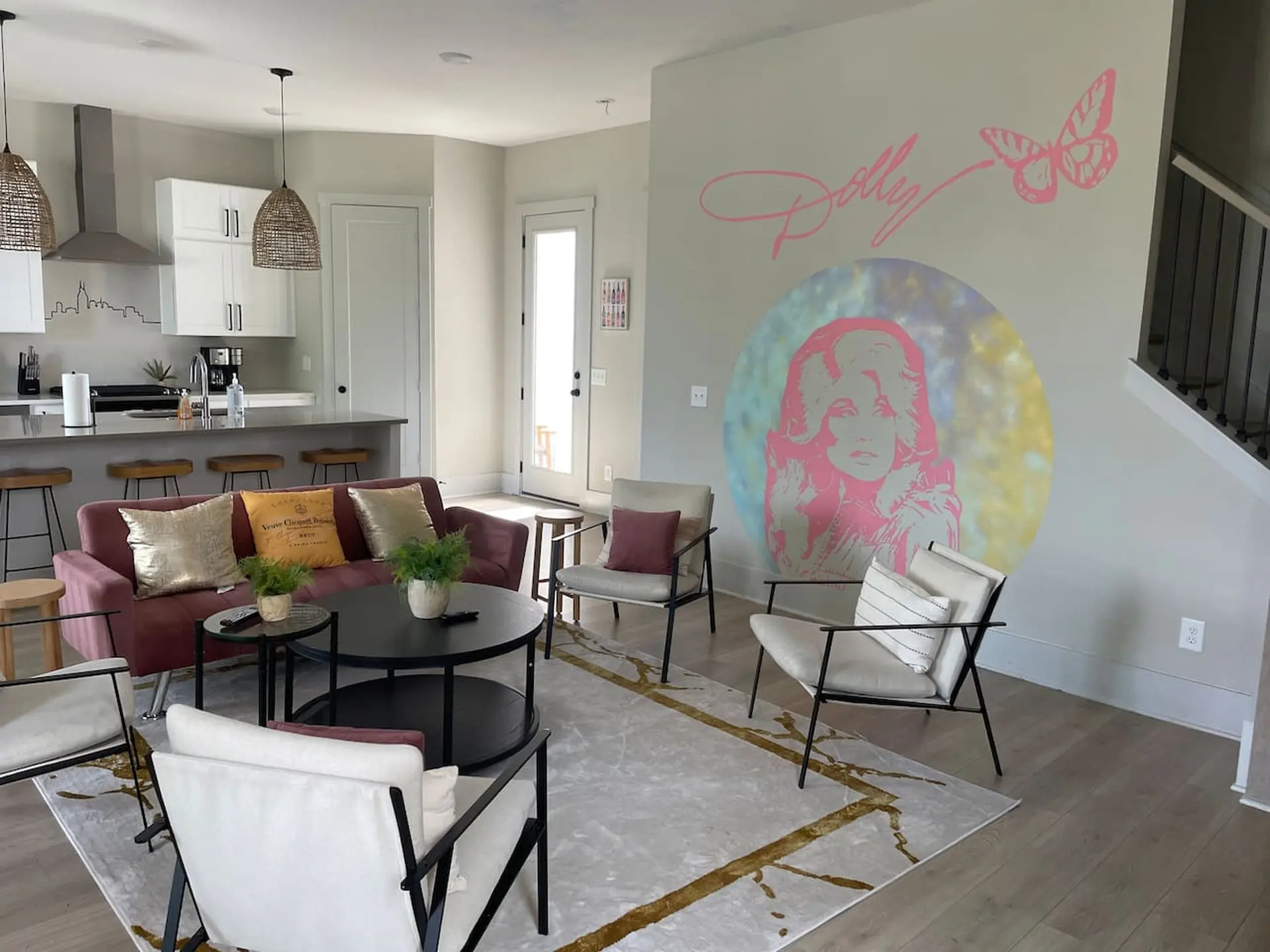 A living room with a pink couch, a Dolly Parton mural, and a kitchen area.