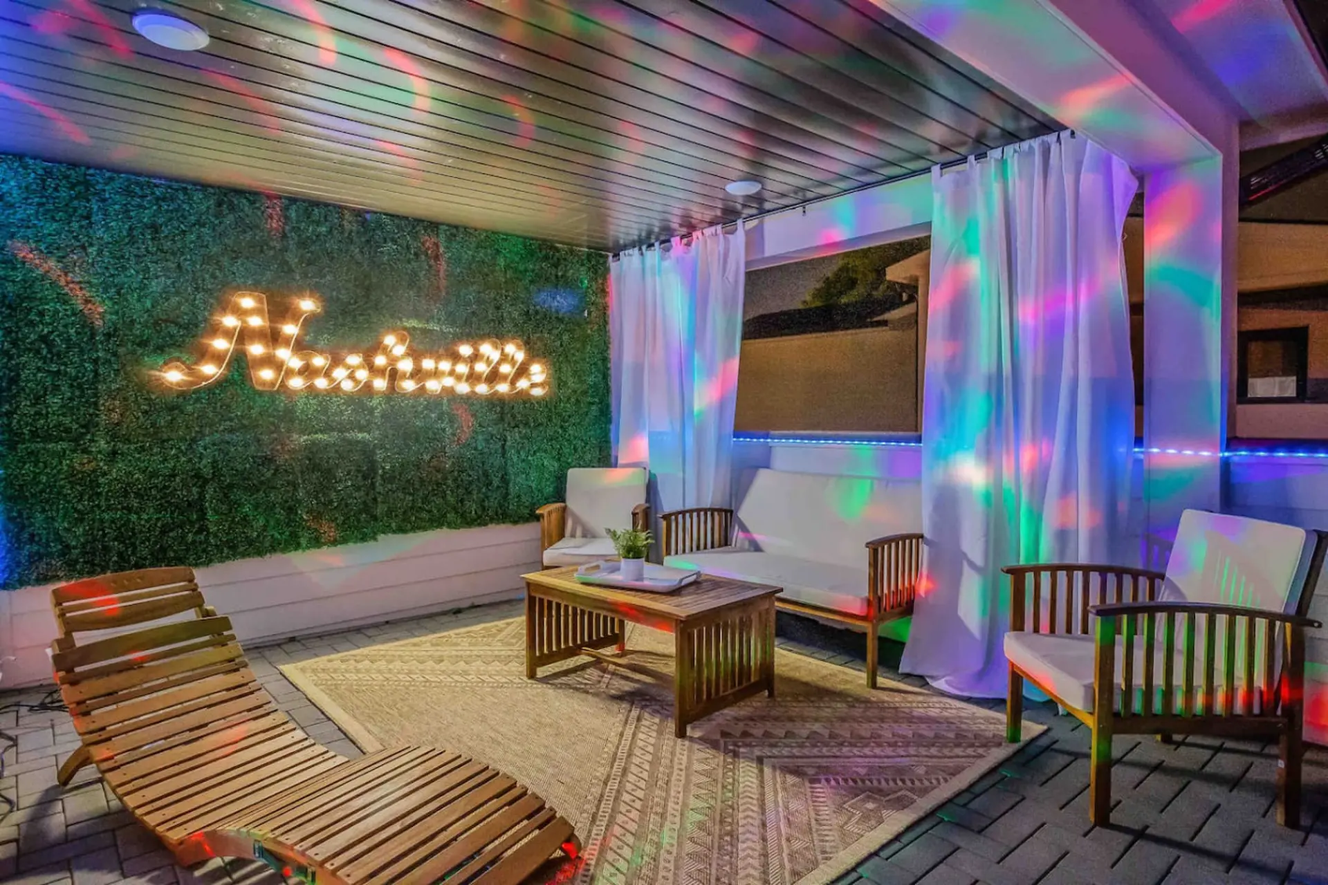 Outdoor patio with a Nashville sign, lounge chairs, sofa, coffee table, and colorful lights.