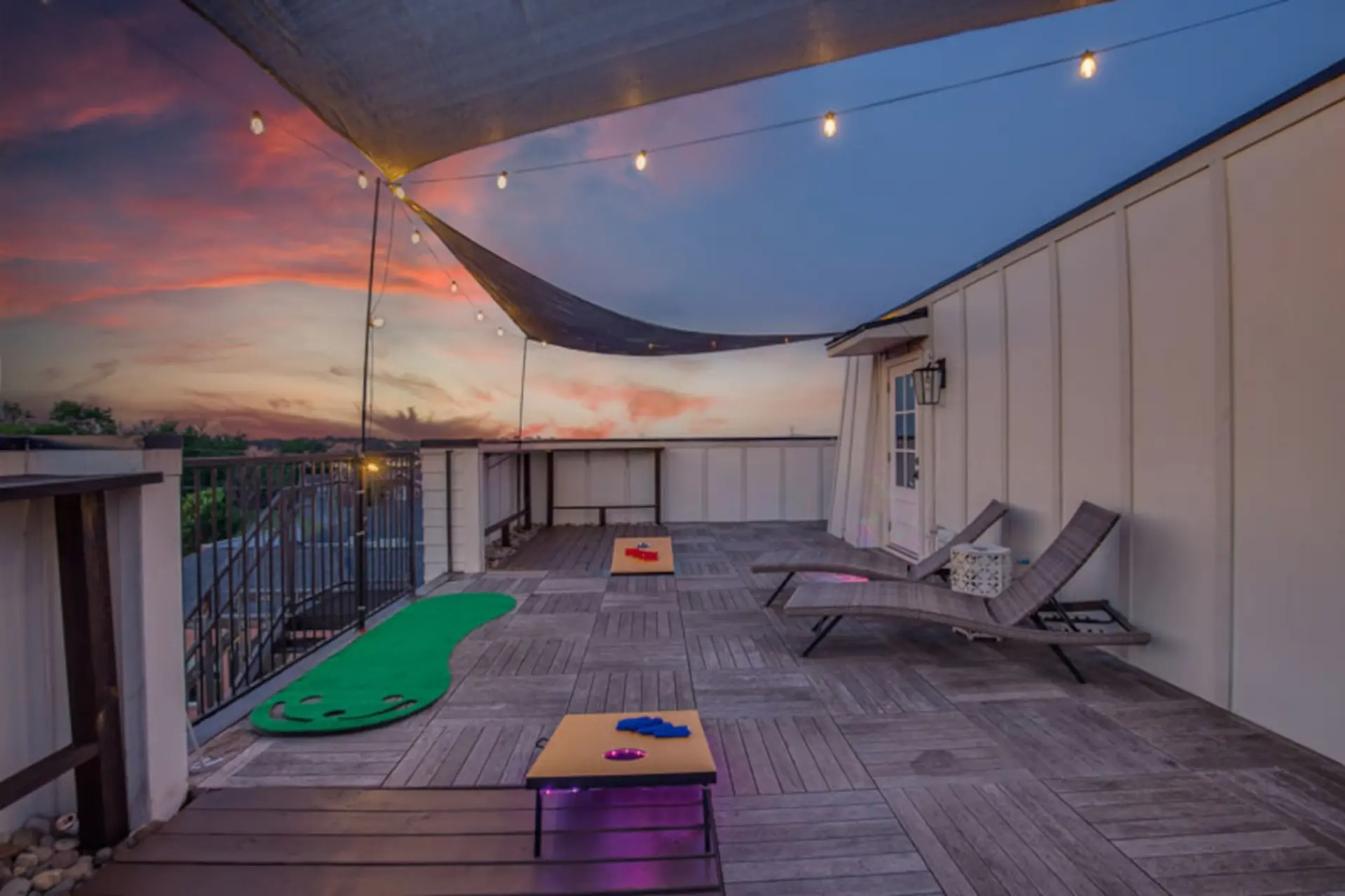 Rooftop deck at sunset with string lights, chaises, and games.