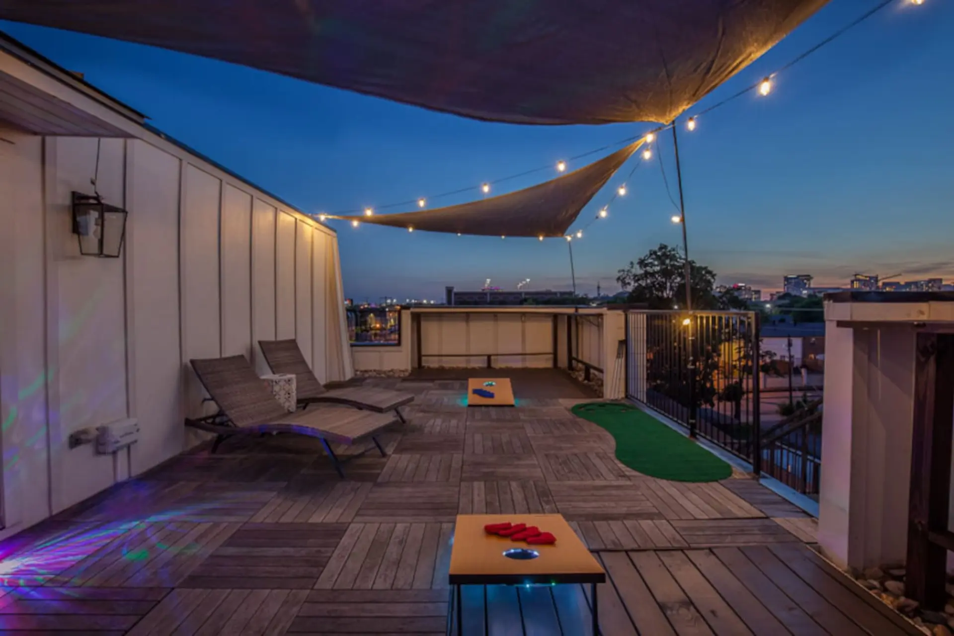 Rooftop patio at dusk with string lights, lounge chairs, and cornhole.
