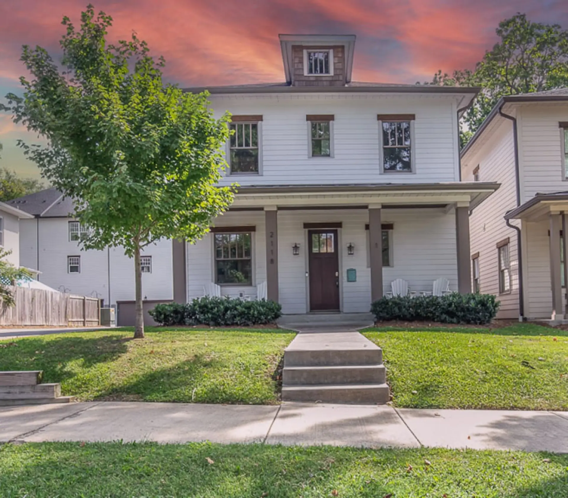 A white two-story house with a porch and a tree in front.