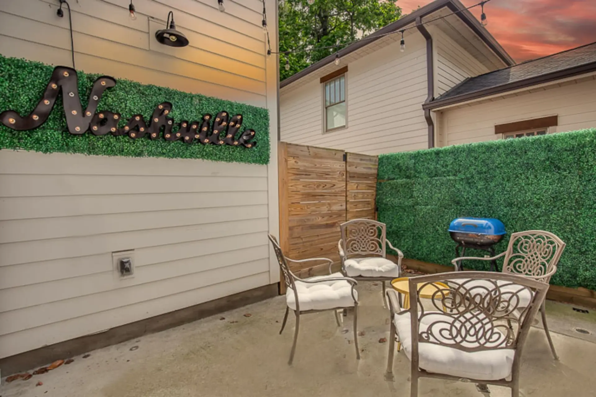 Patio with faux-grass wall, ornate chairs, a grill, and "Nashville" marquee sign.