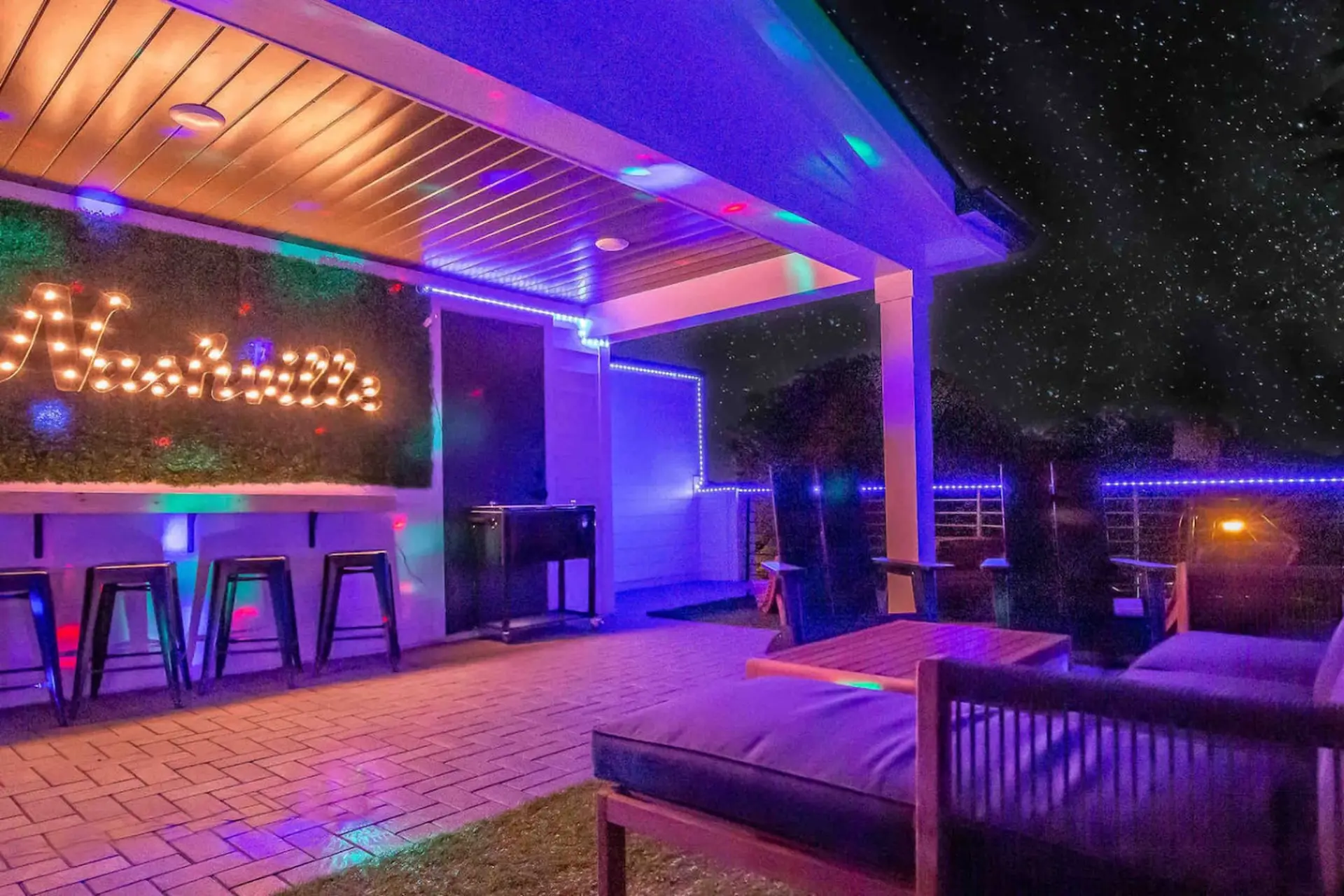 Backyard patio with string lights, bar stools, and a "Nashville" marquee sign.