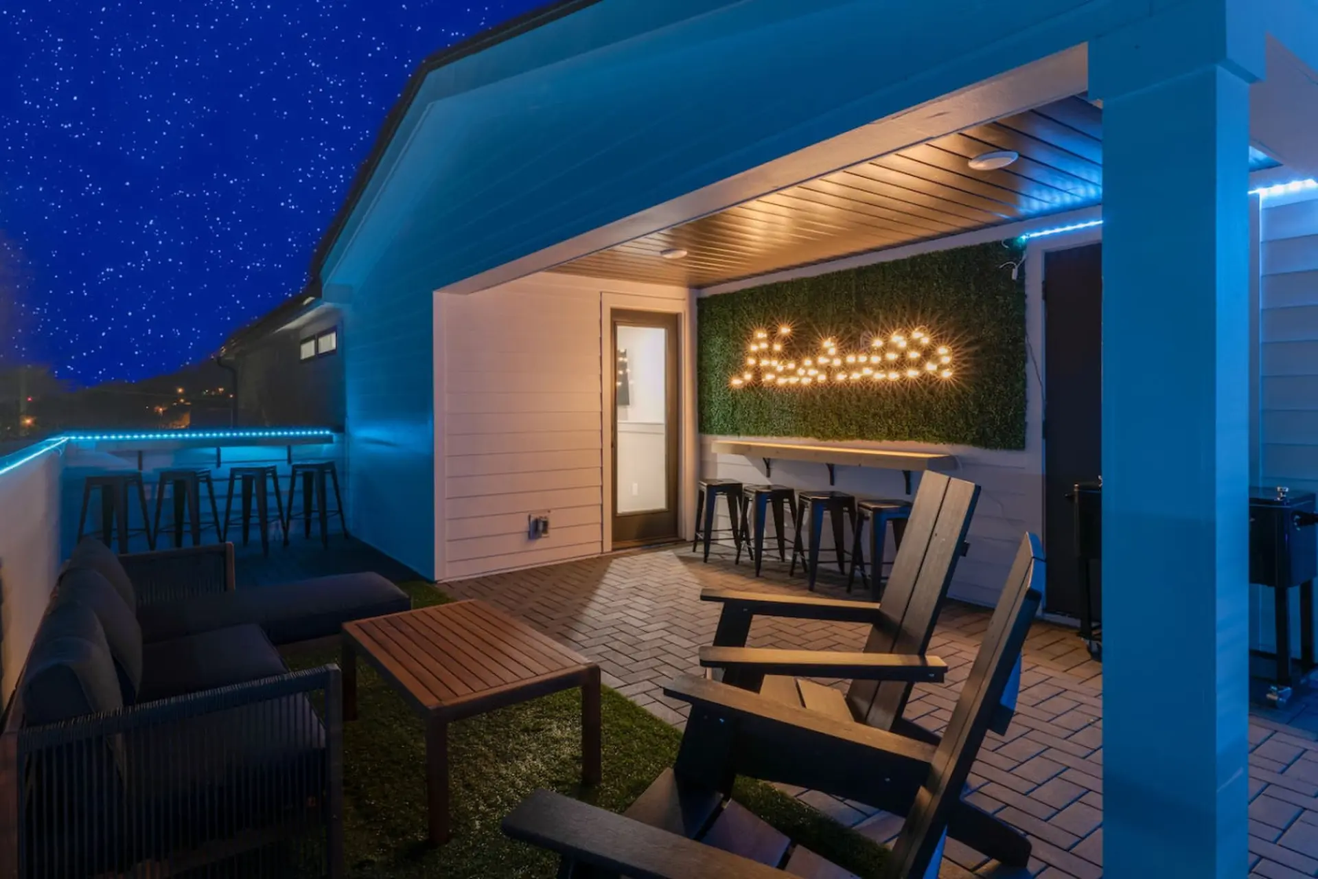 An outdoor patio with lounge seating and a bar area lit by string lights at night.