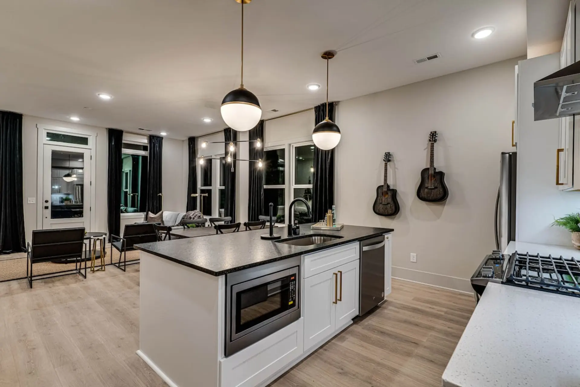 A modern kitchen island with a microwave and dishwasher in a bright room with guitars on the wall.