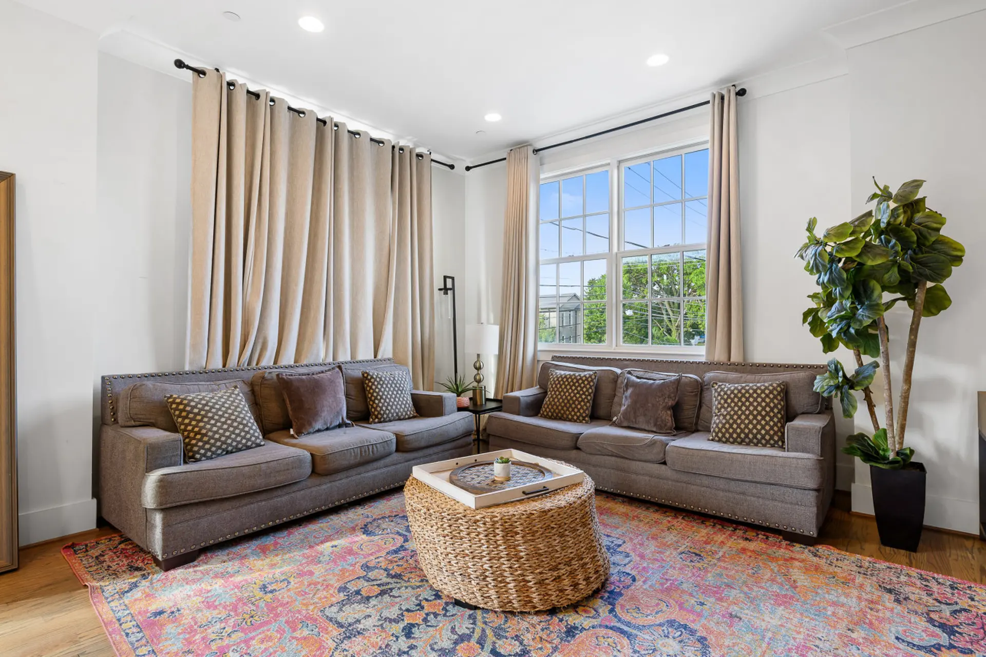 A living room with two gray sofas, a woven ottoman, and a large potted plant.