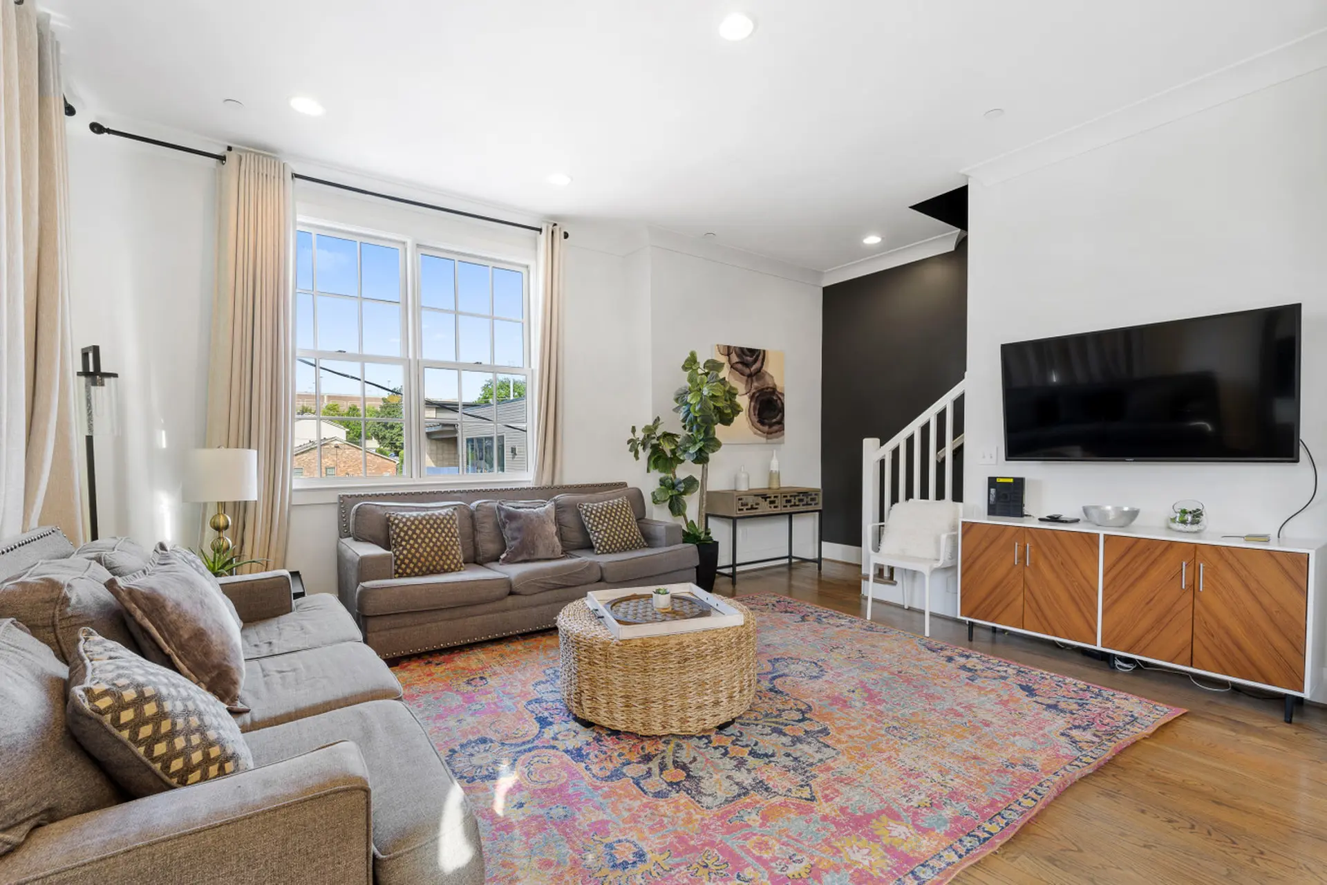 A bright living room with a large sectional couch, patterned rug, and television.