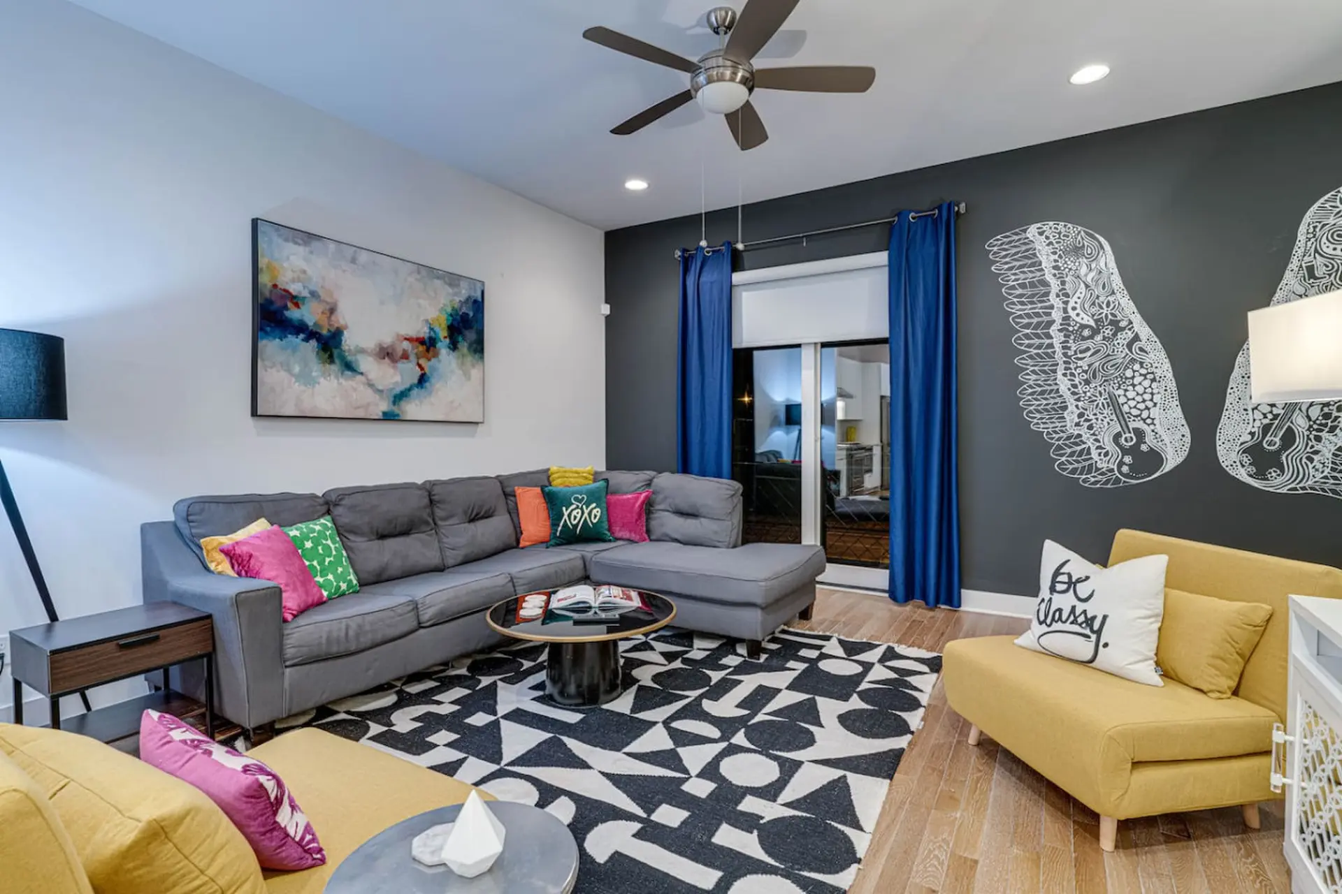 A modern living room with a gray sectional, yellow chairs, and abstract art.