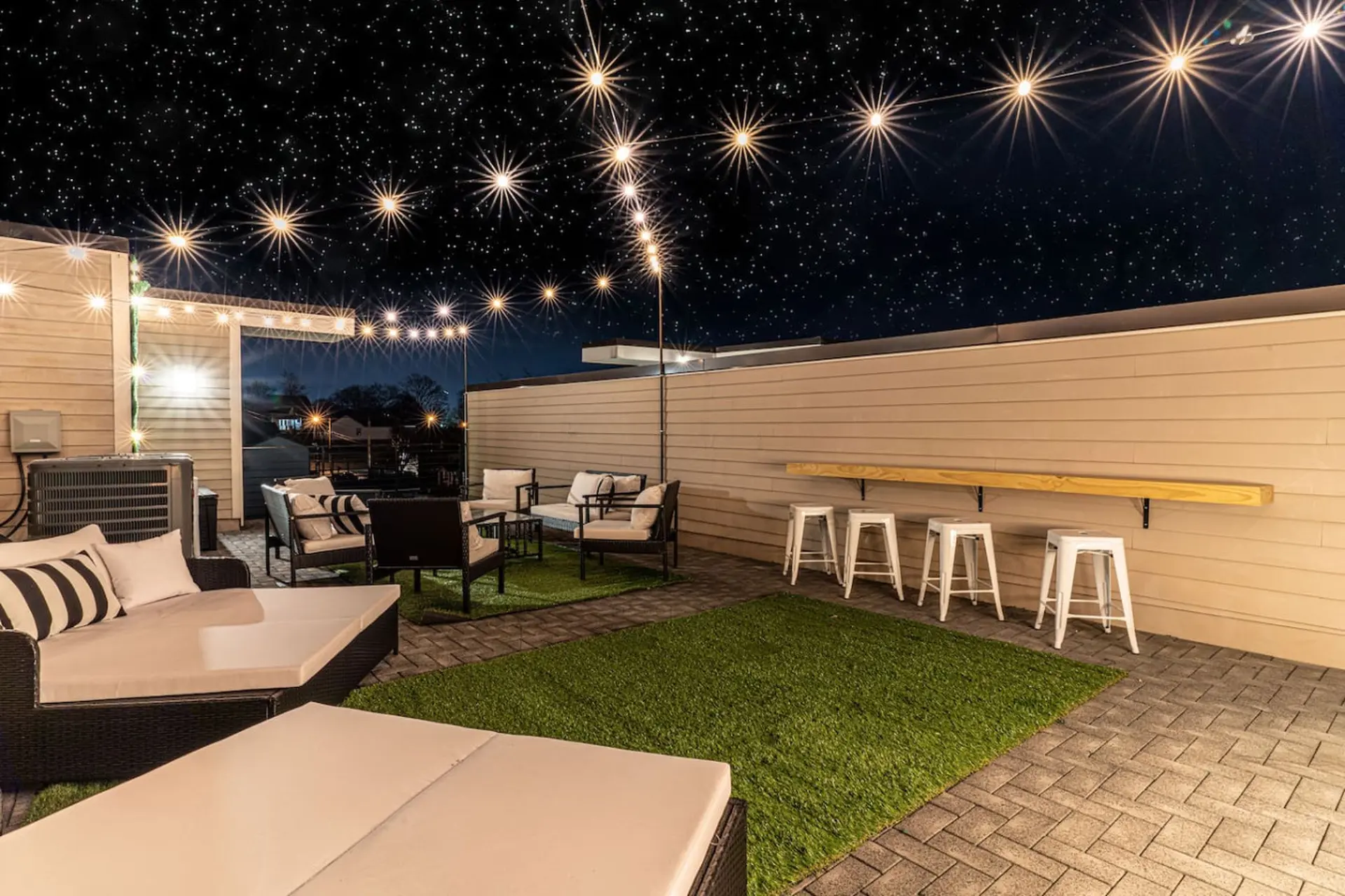 Outdoor patio with lounge seating and a bar with stools under a starry sky with string lights.