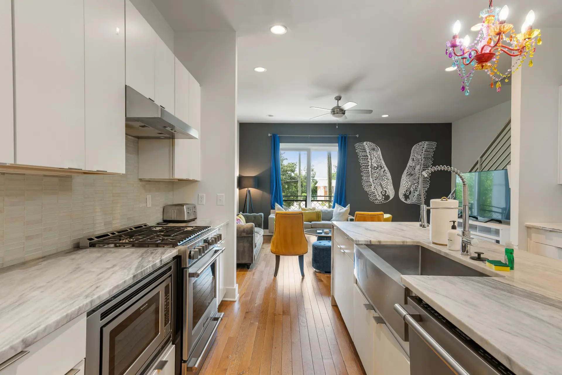 Modern open-plan kitchen with stainless steel appliances, marble countertops, and a living area with