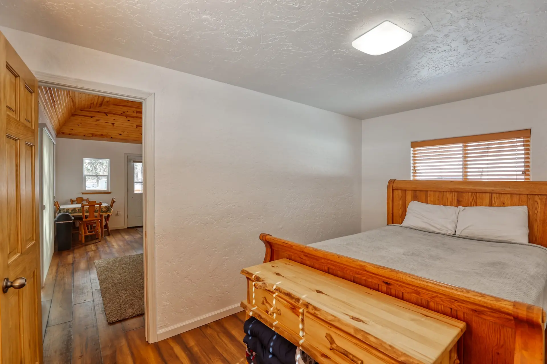 Bedroom with a wooden bed, a chest, and a doorway leading to a dining area.