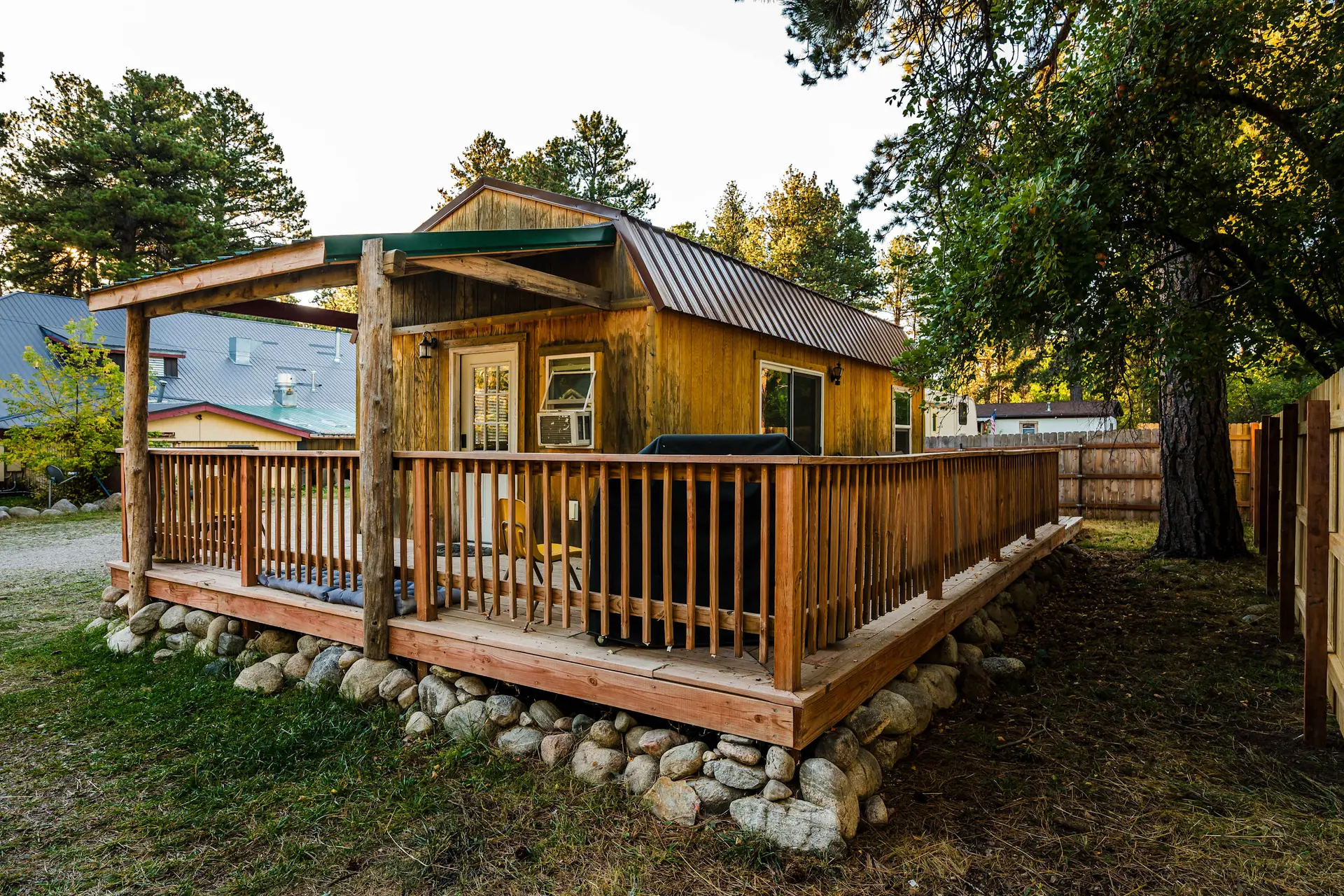 A rustic cabin with a wooden deck and a metal roof sits among trees.