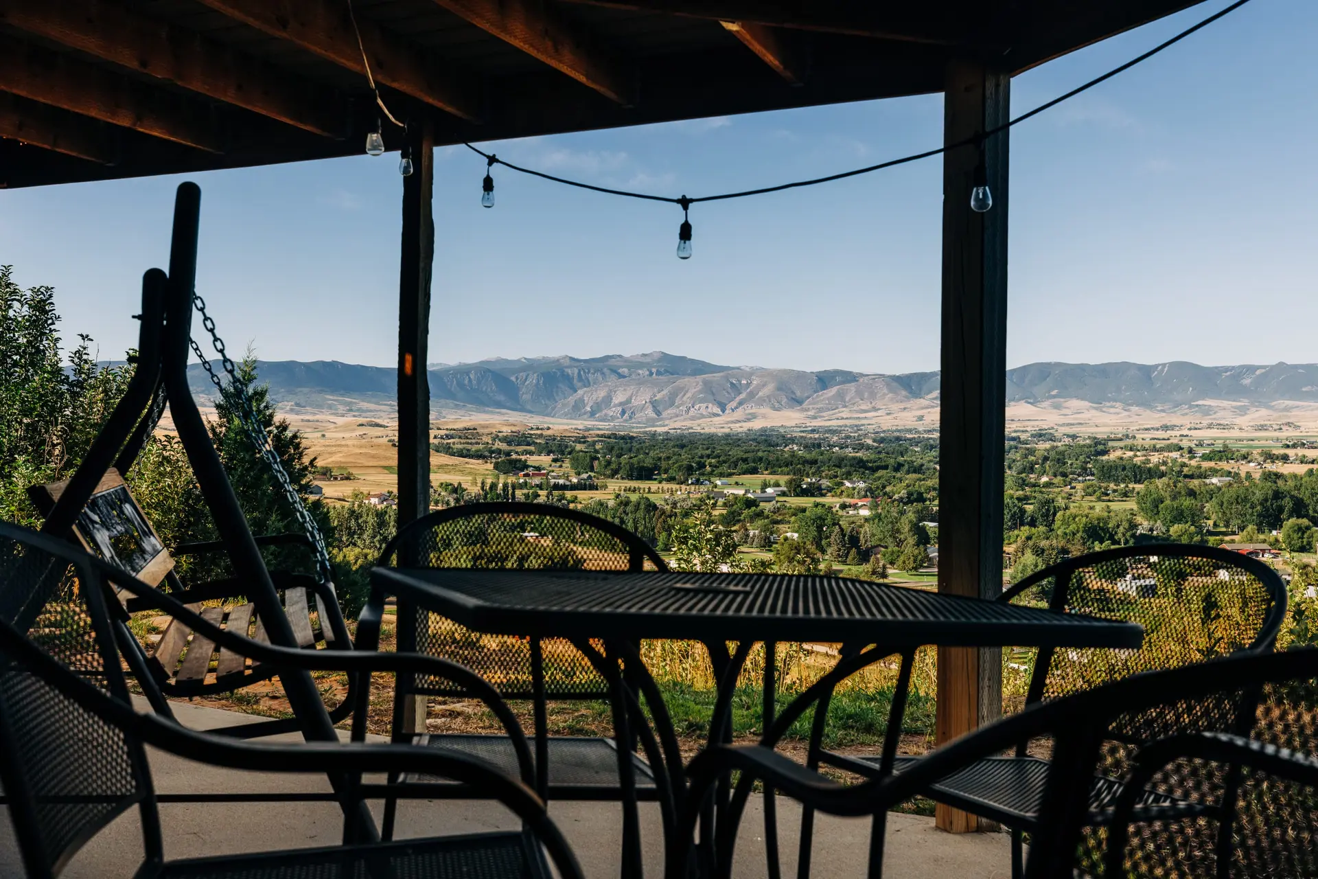 Outdoor patio with chairs and table facing a scenic valley and mountains.