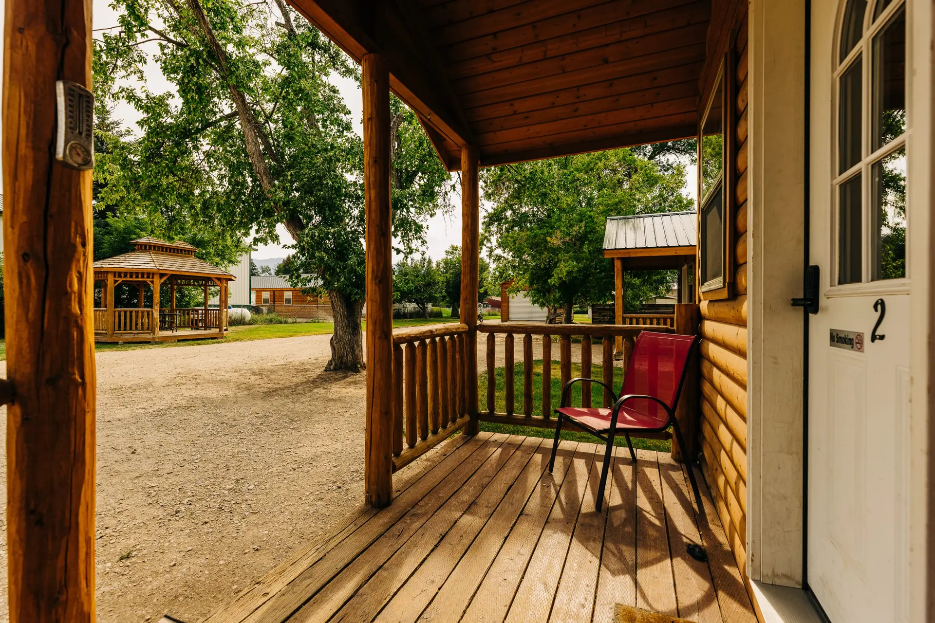 A wooden porch with a red chair and a view of a gazebo and trees.