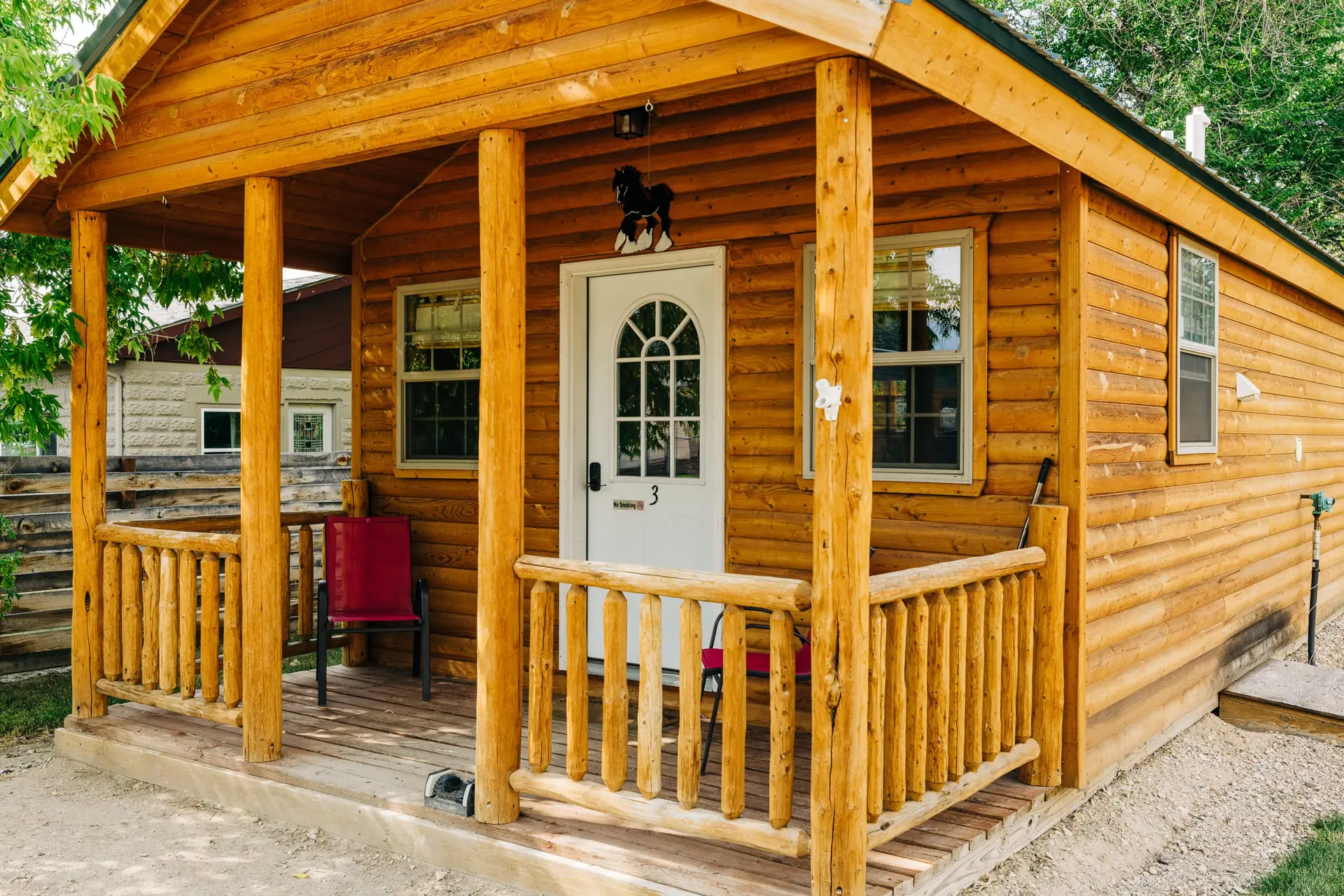 Rustic log cabin with a porch and red chairs.