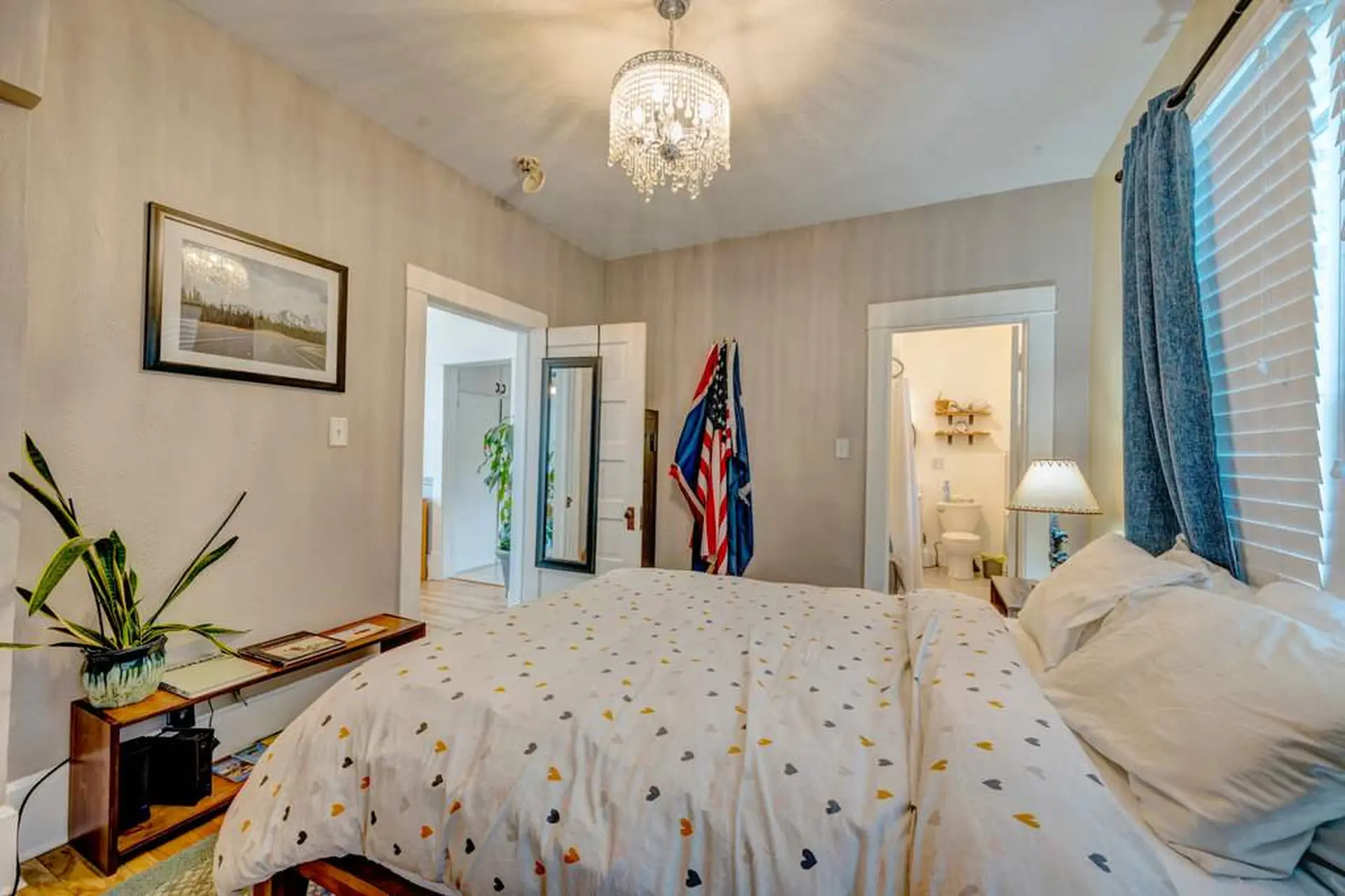 Bedroom with a chandelier, framed art, a flag, and a bed with a heart-patterned duvet.