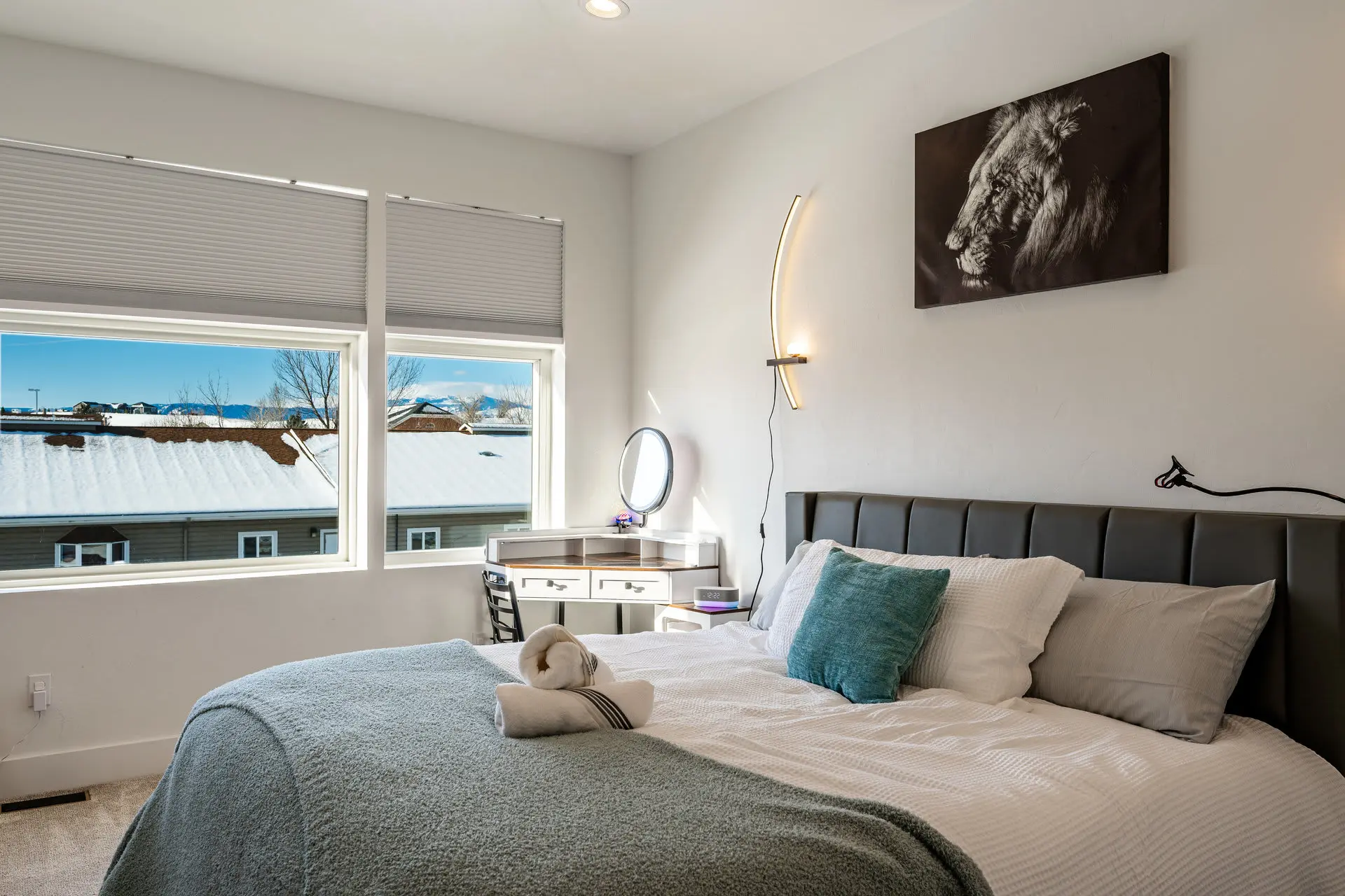 A bed with a headboard, pillows, and a blanket, near a desk and a window with a snowy view.