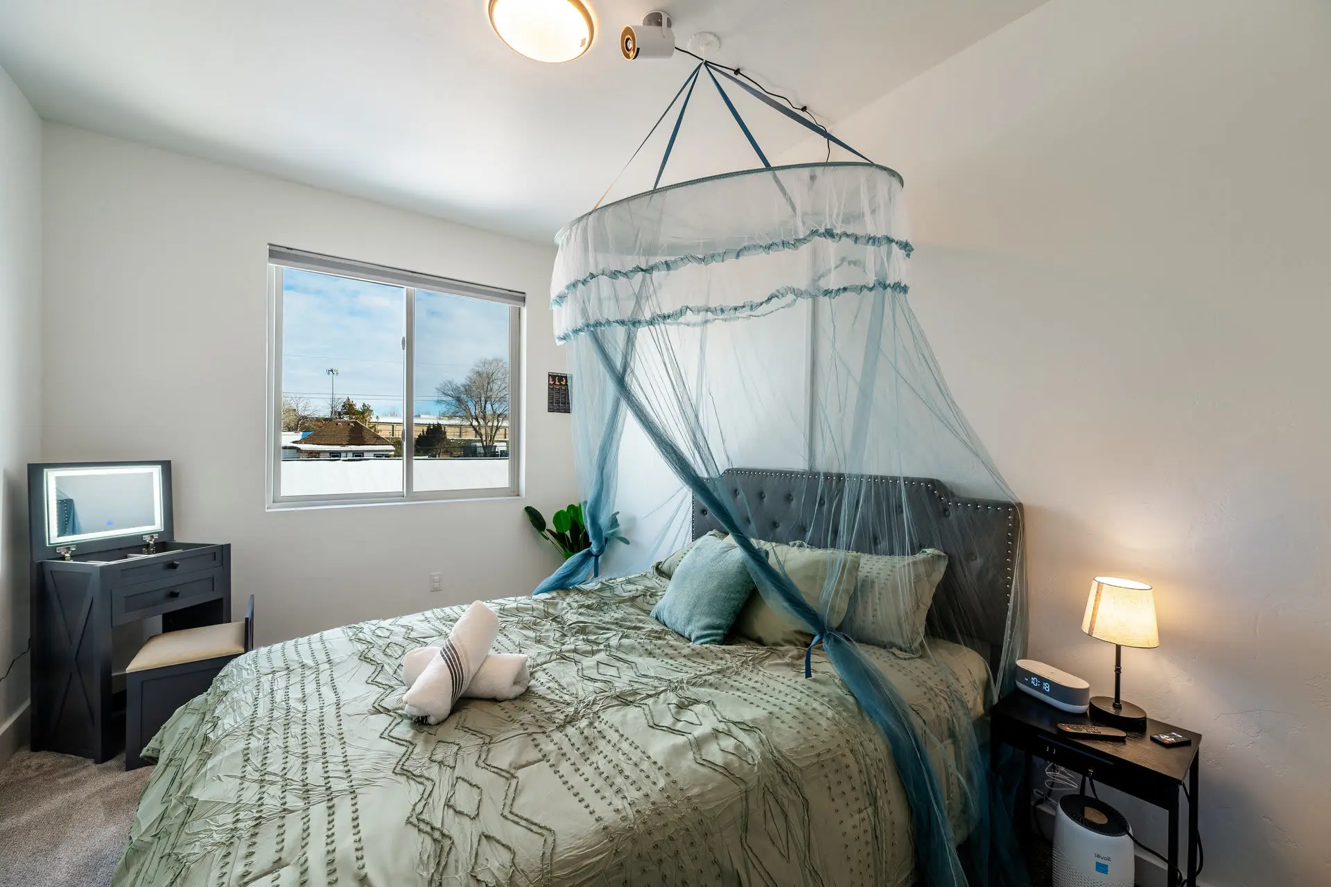 A bedroom with a bed, vanity, and window.
