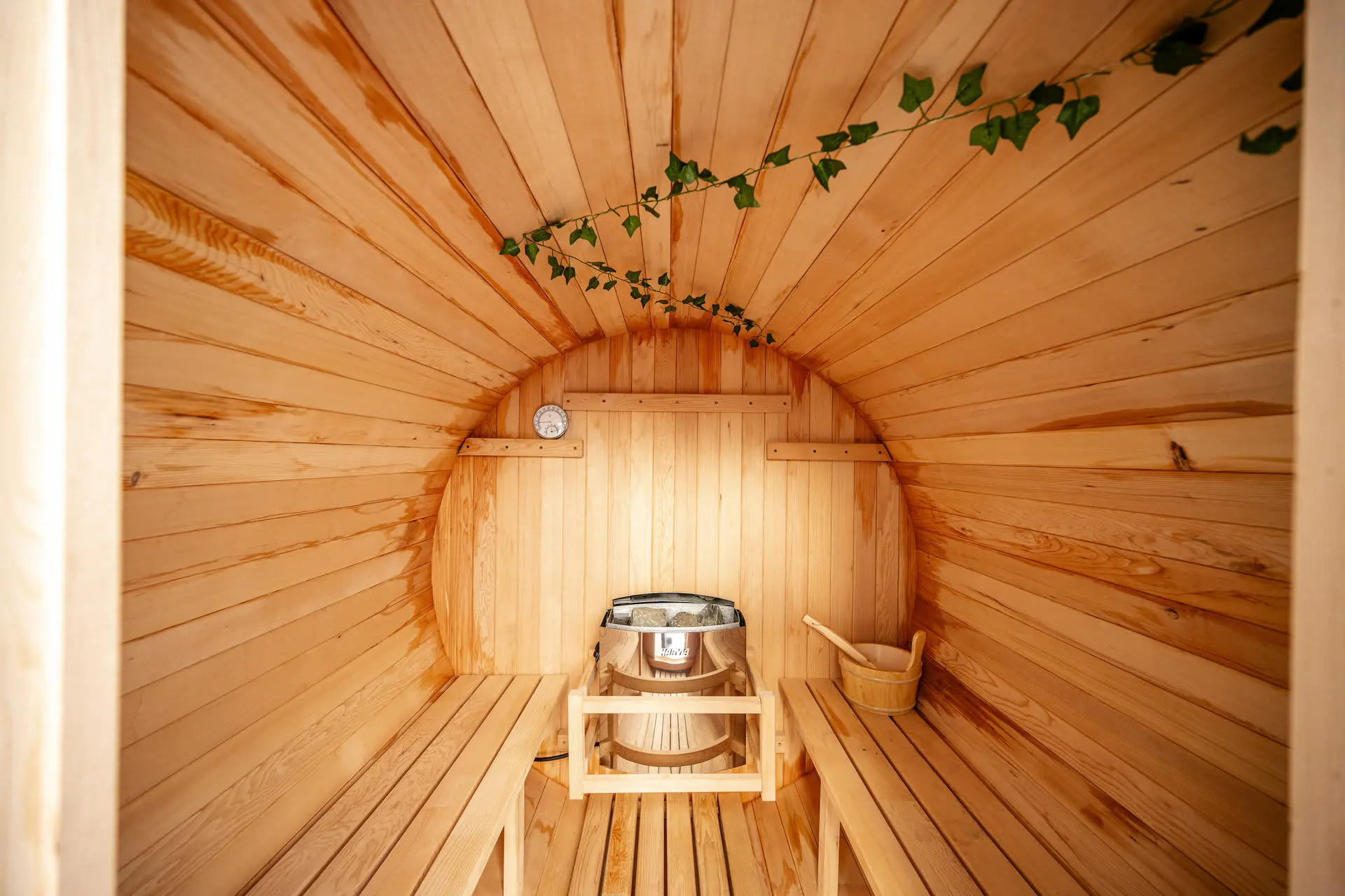 Wooden barrel sauna interior with a heater, benches, and a thermometer.