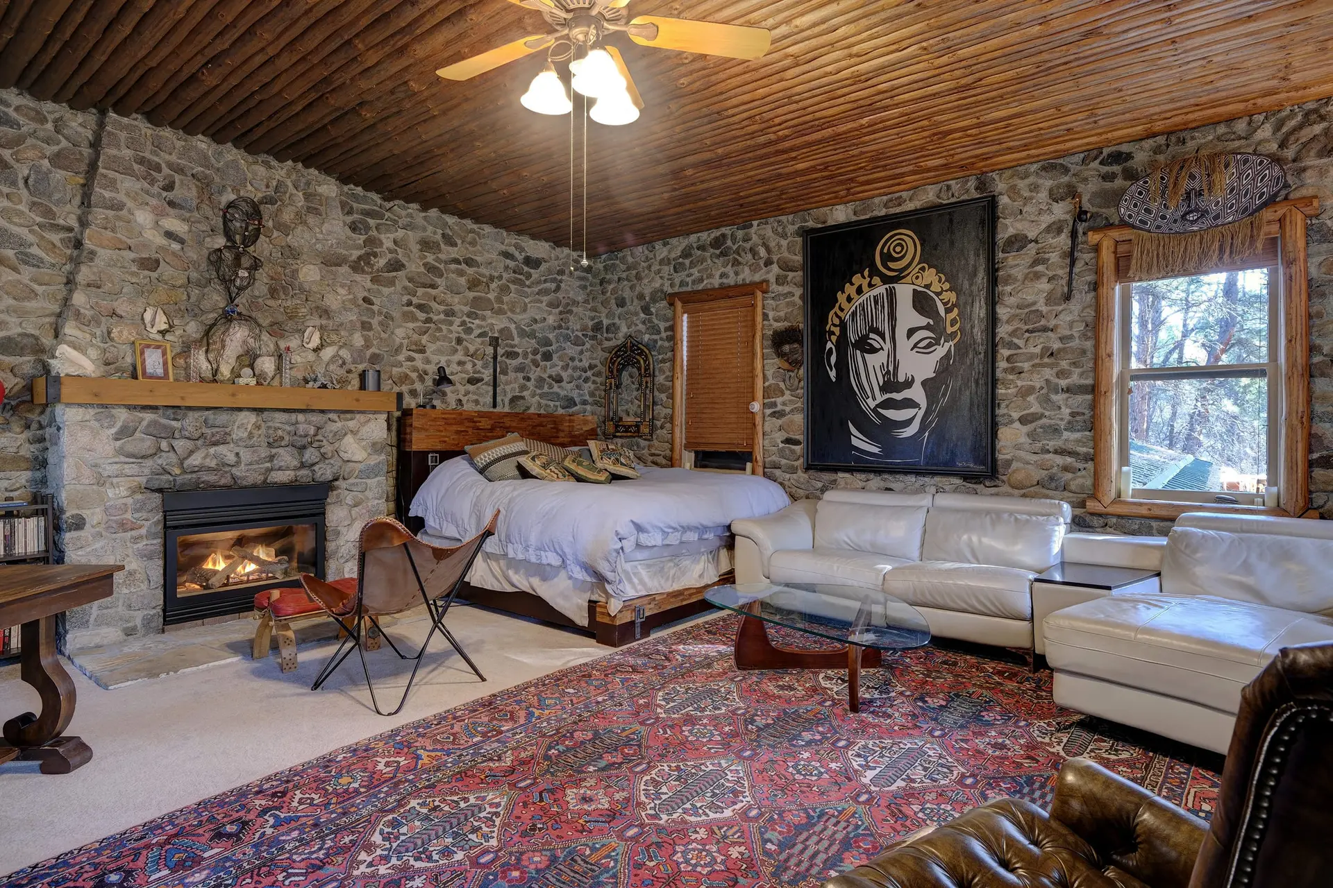 A rustic bedroom with stone walls, a wooden ceiling, and a large painting.