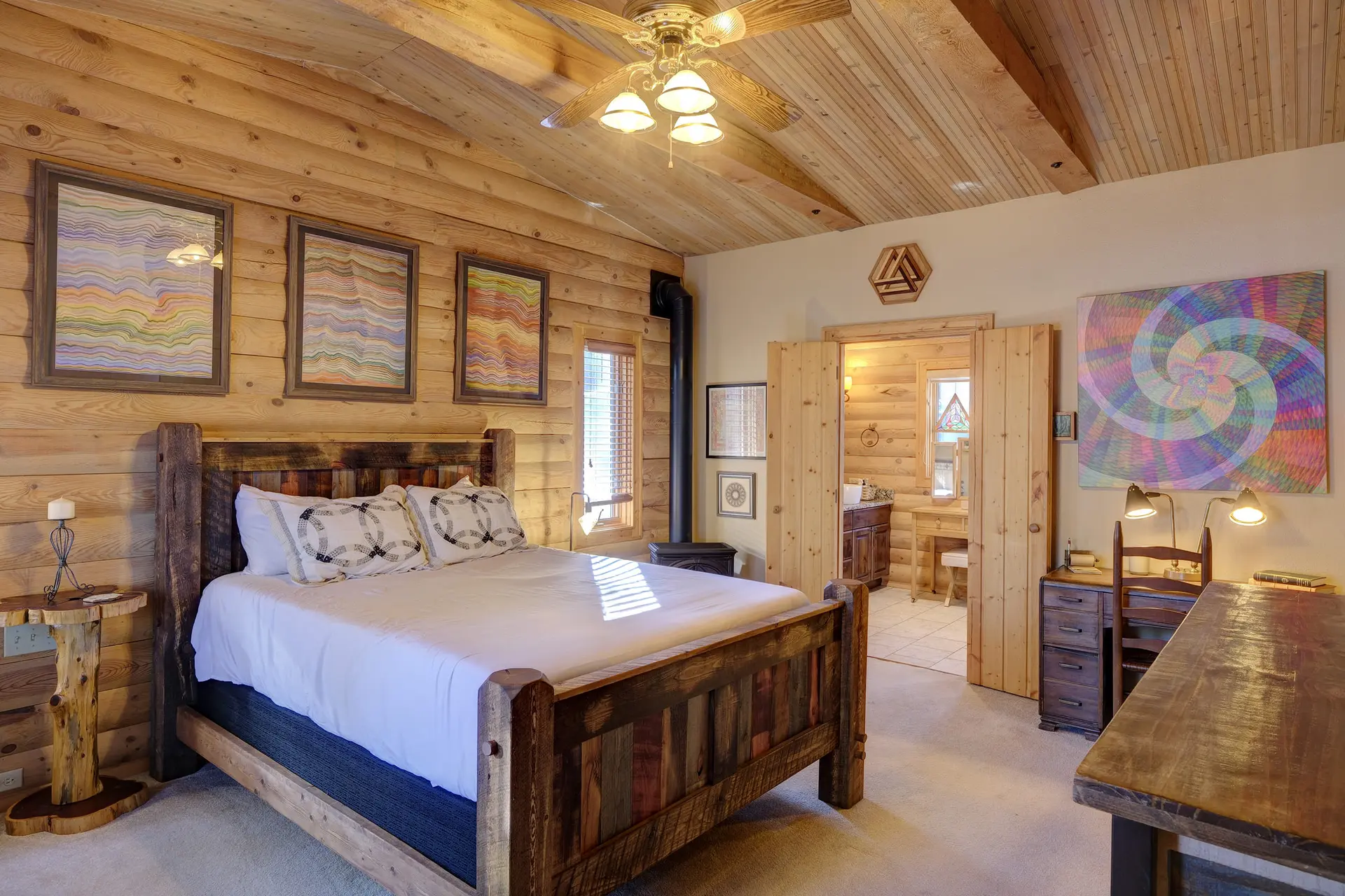 A rustic bedroom with log walls and ceiling, a wood bed, and colorful artwork.