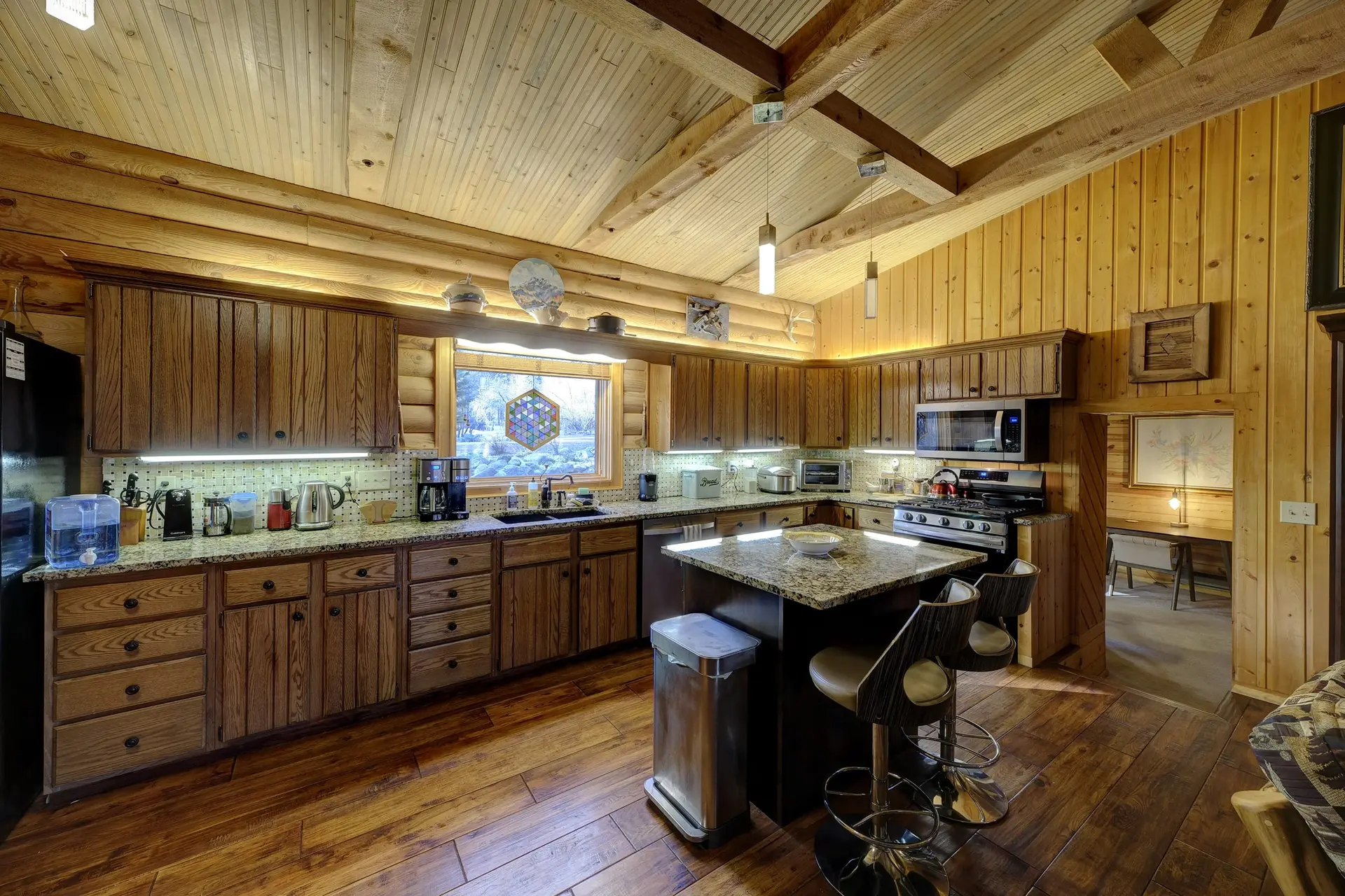 A cozy log cabin kitchen with wood cabinets, granite countertops, and a large island.