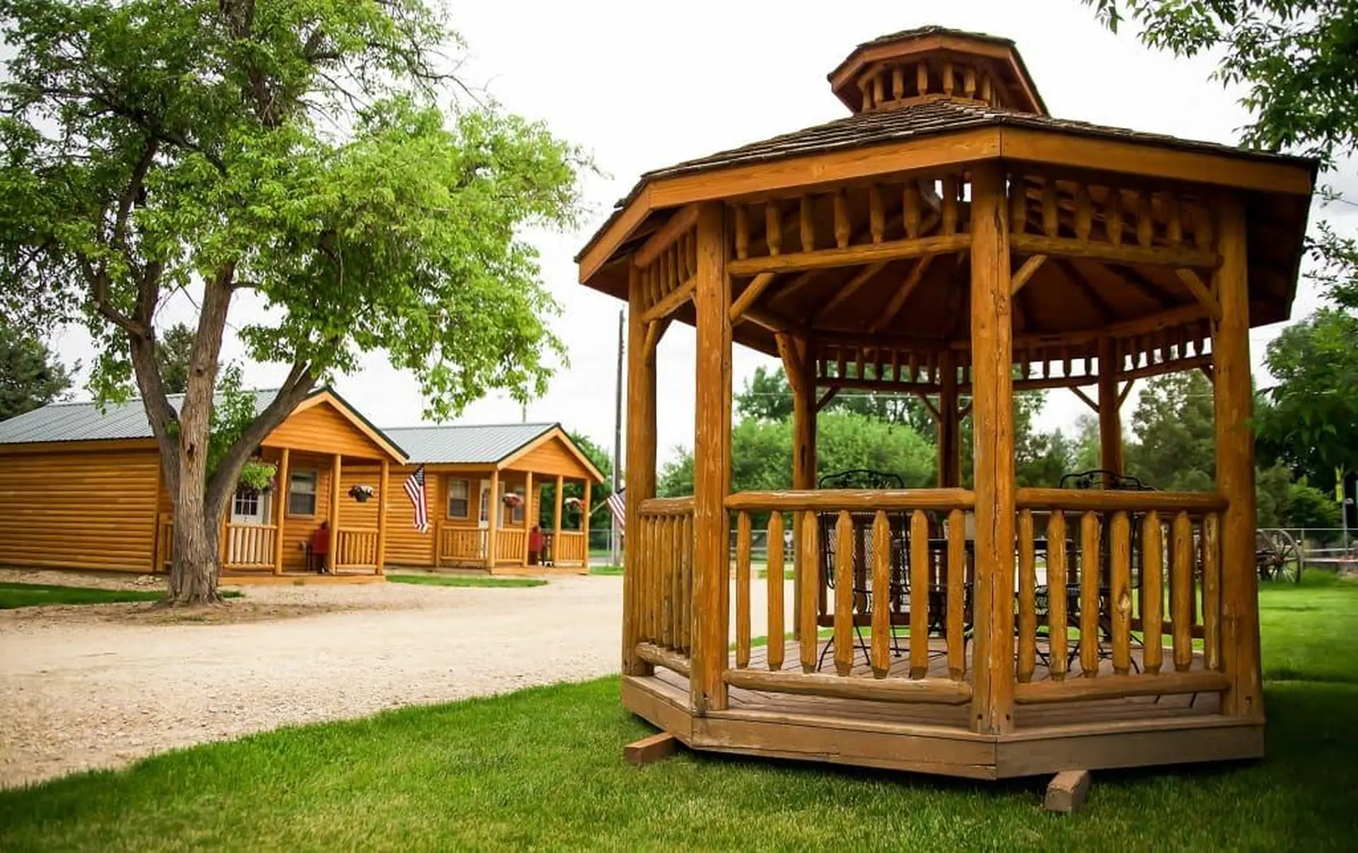 A wooden gazebo and log cabins in a grassy area.