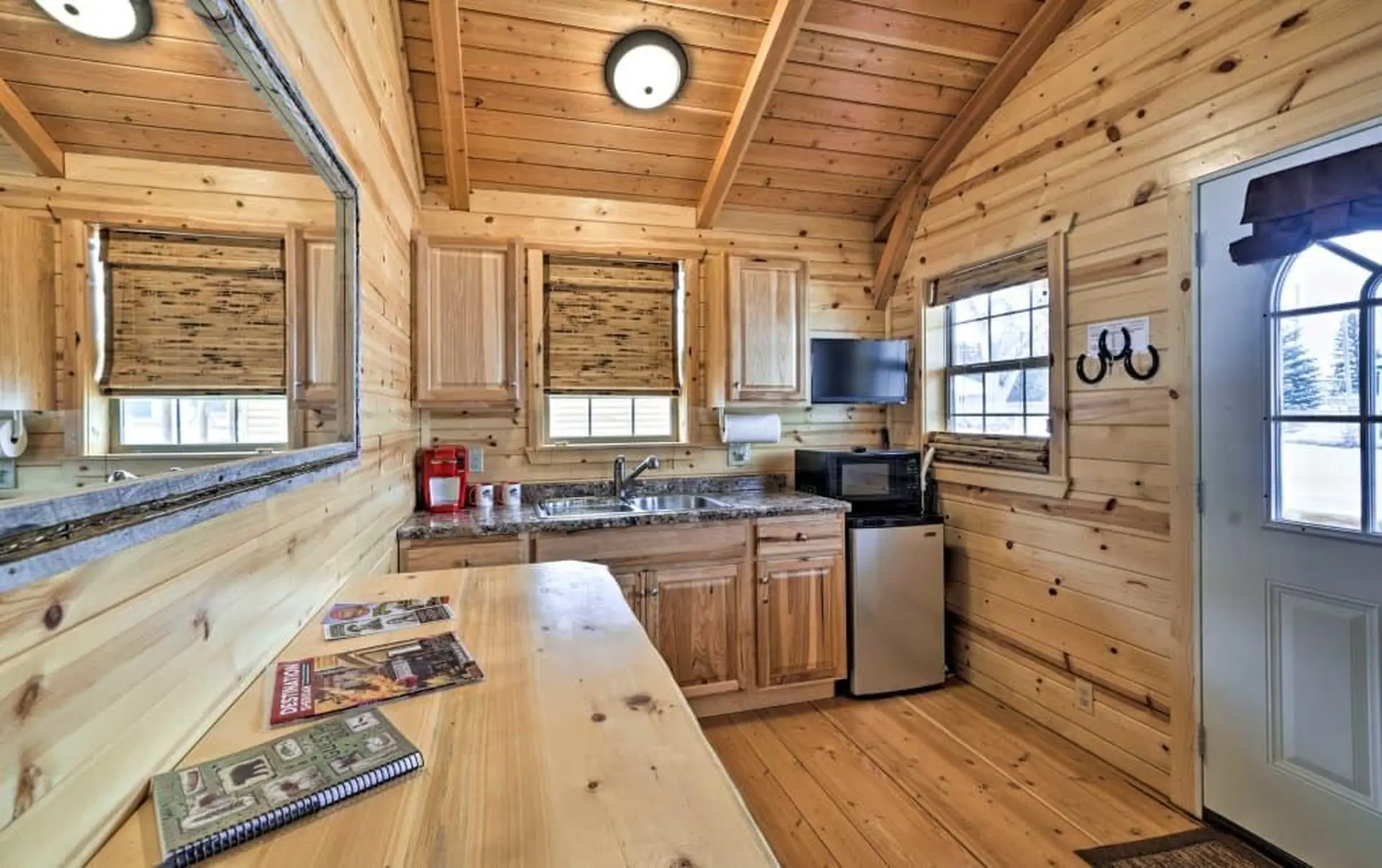 Cozy cabin kitchen with wood interior, a sink, microwave, mini-fridge, and a table with magazines.