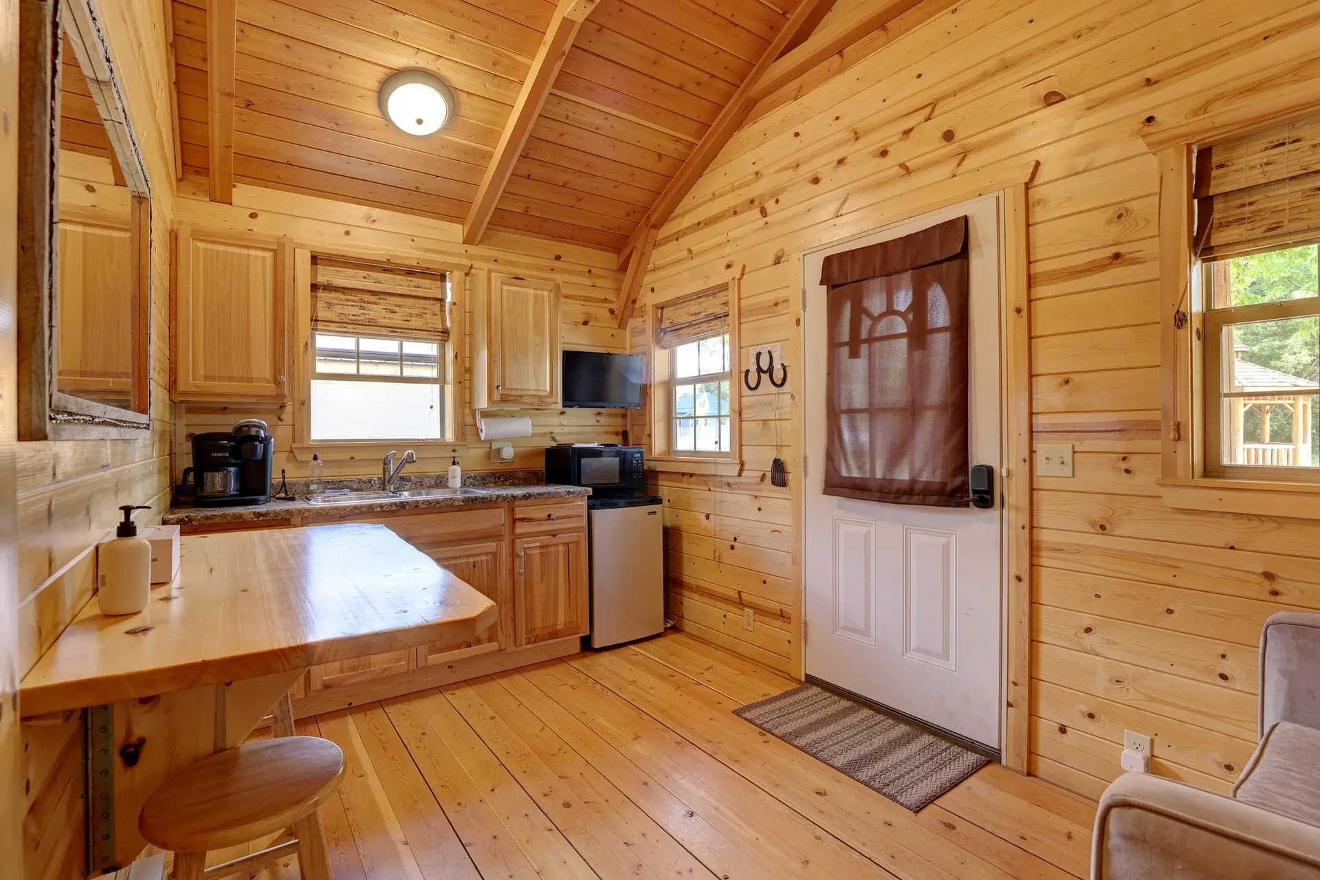 A cozy cabin kitchen featuring wooden walls, a sink, a microwave, and a coffee maker.