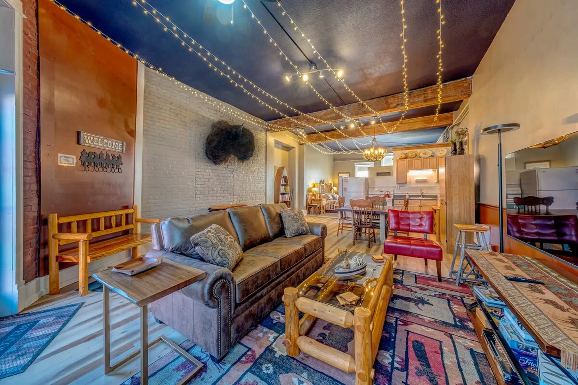 A rustic living room with a brown leather couch, log coffee table, and string lights on the ceiling.