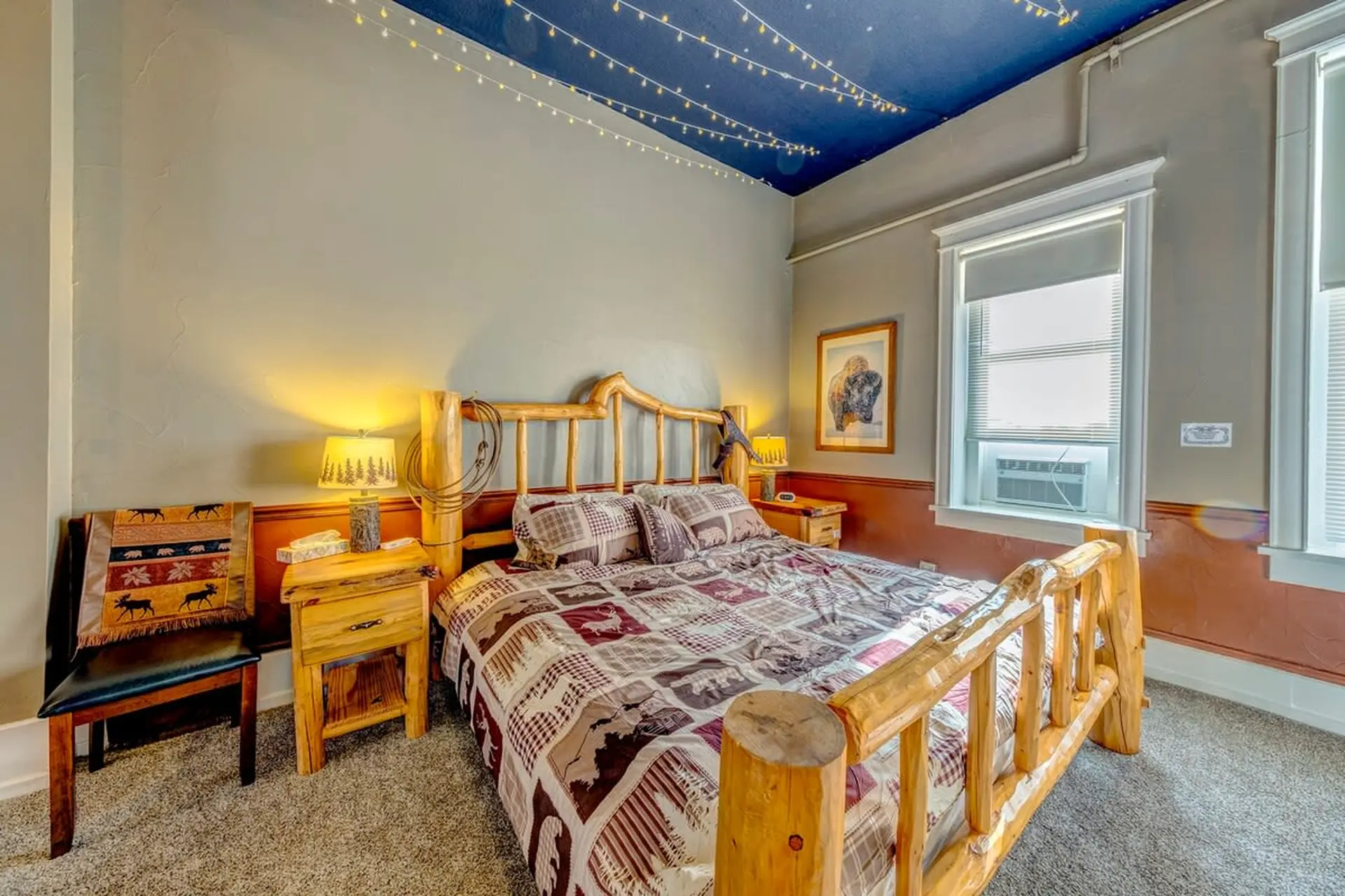 A rustic wooden bed with a patchwork quilt and a framed buffalo hangs on the wall.