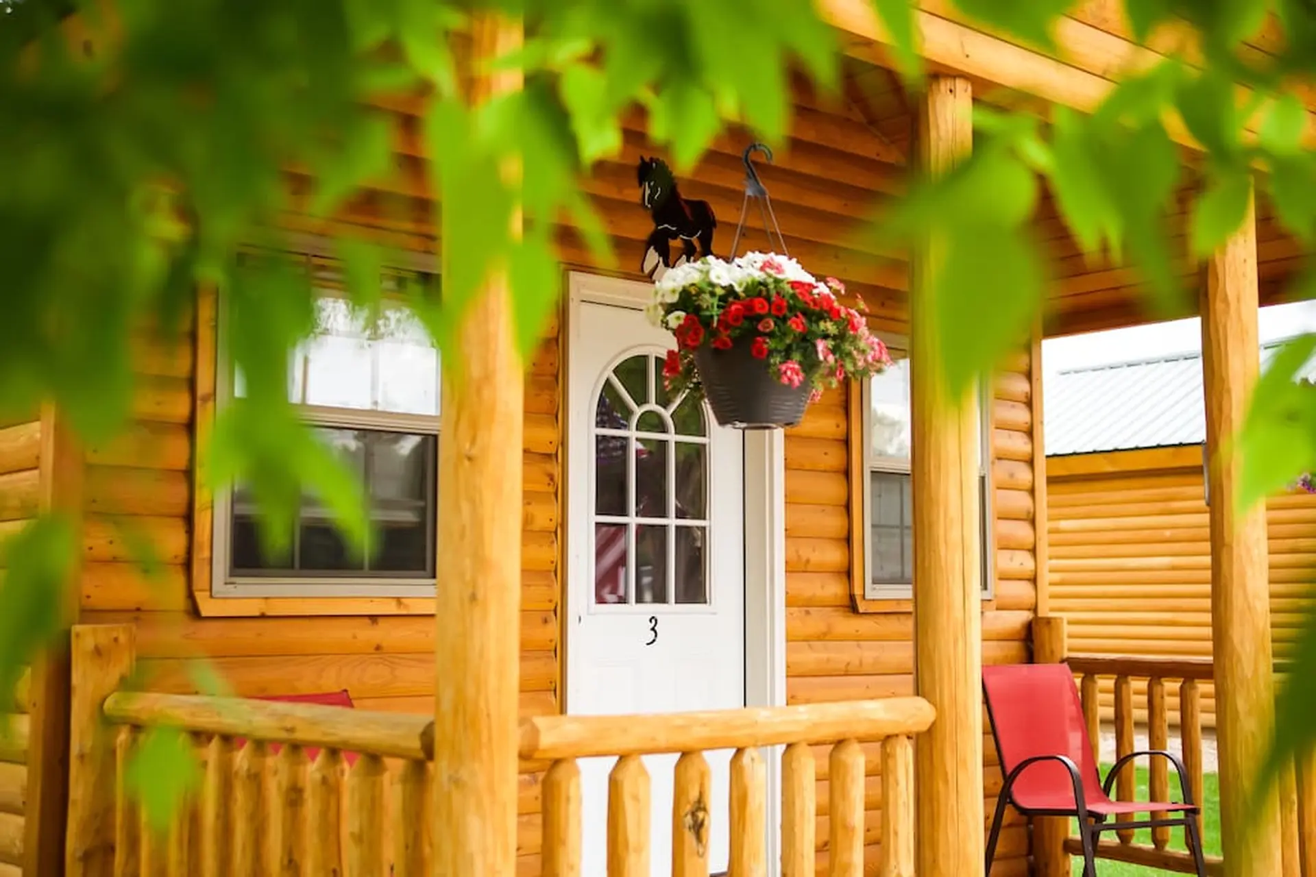 A cabin with a porch, flowers, and two red chairs.