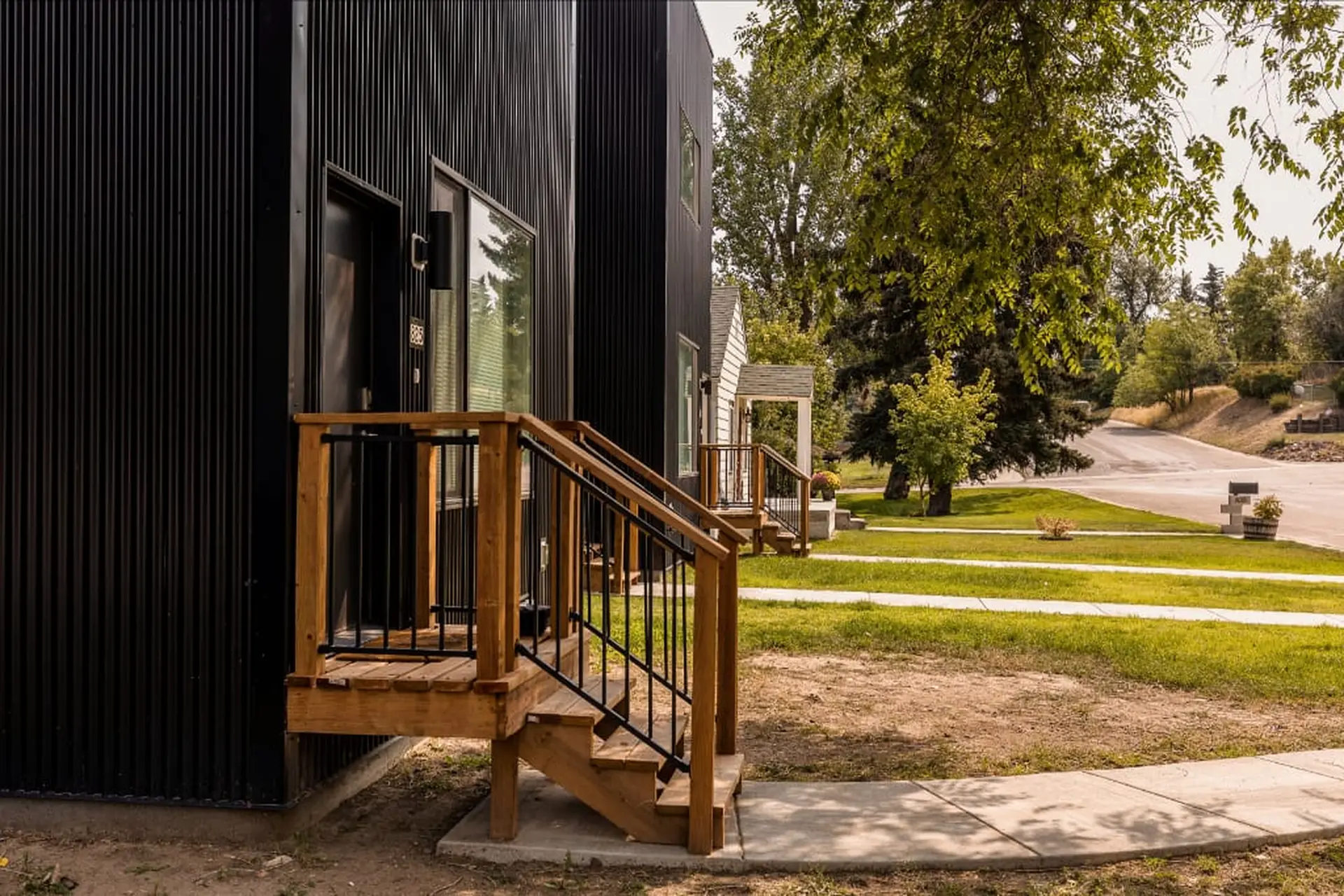 A modern black house with wooden steps and railings, surrounded by a green lawn and trees.