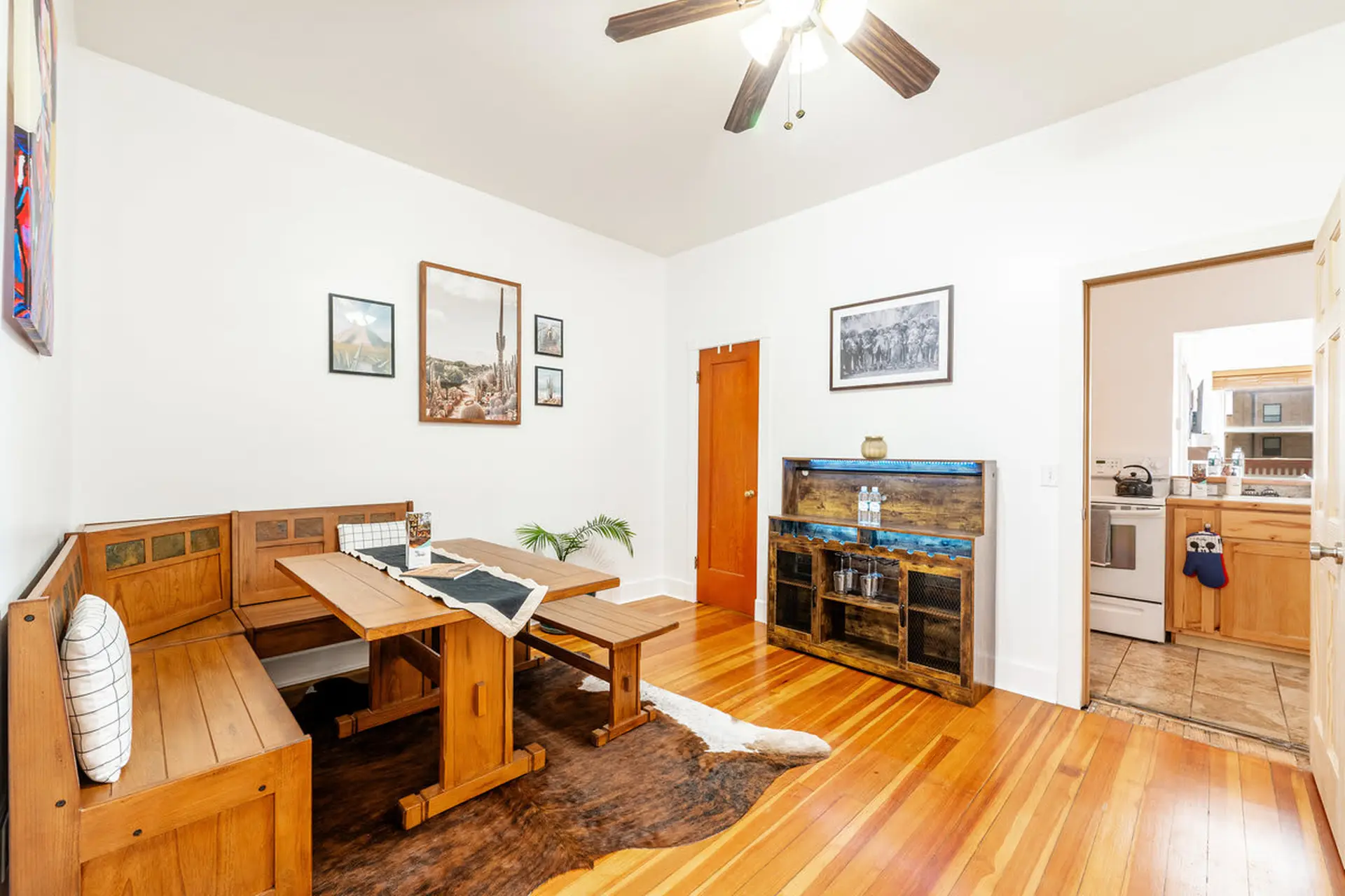 A dining area with a wooden banquette, table, and bench, and a cabinet with bottles and glasses.