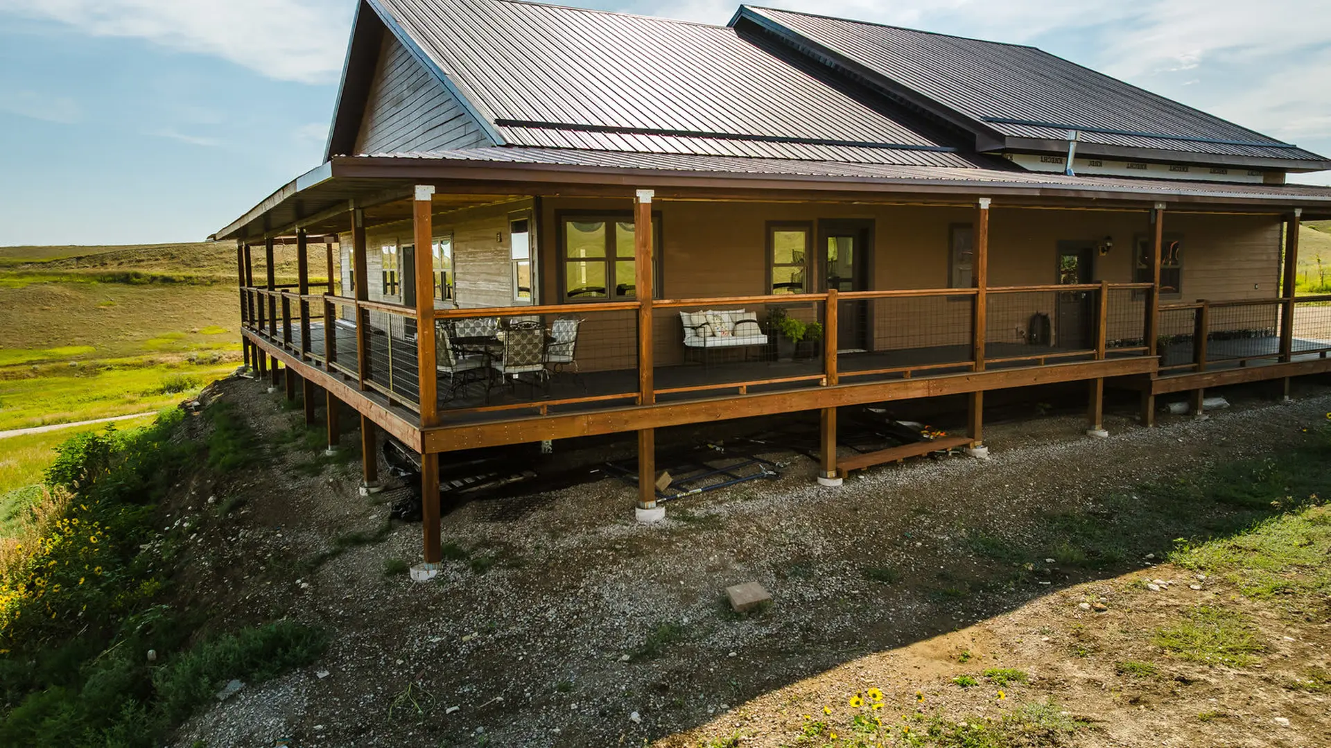A modern house on a hill with a large wooden deck and a metal roof.