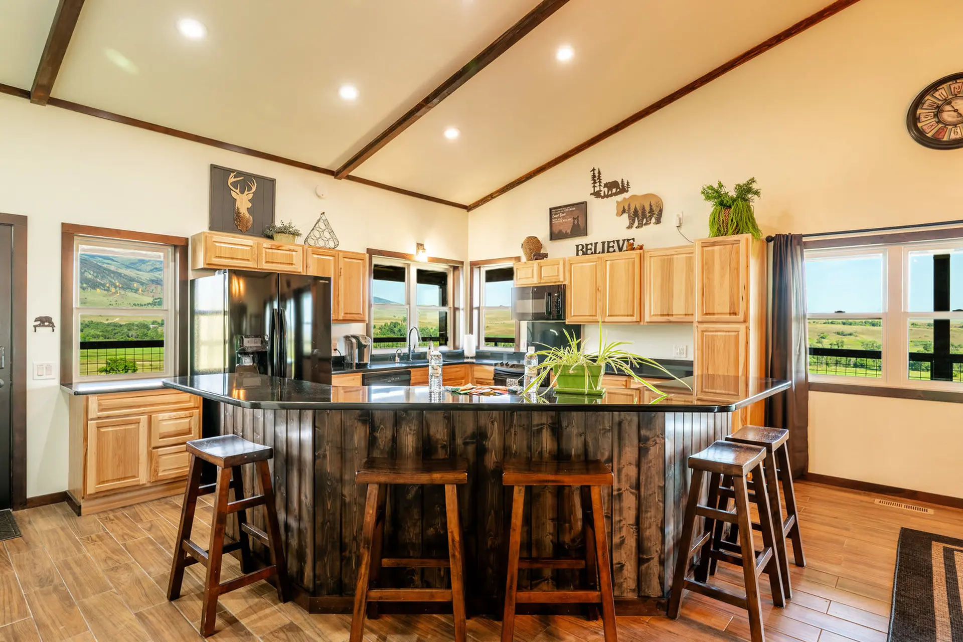 A modern kitchen with wood cabinets and a dark wood island features natural light and a scenic view.
