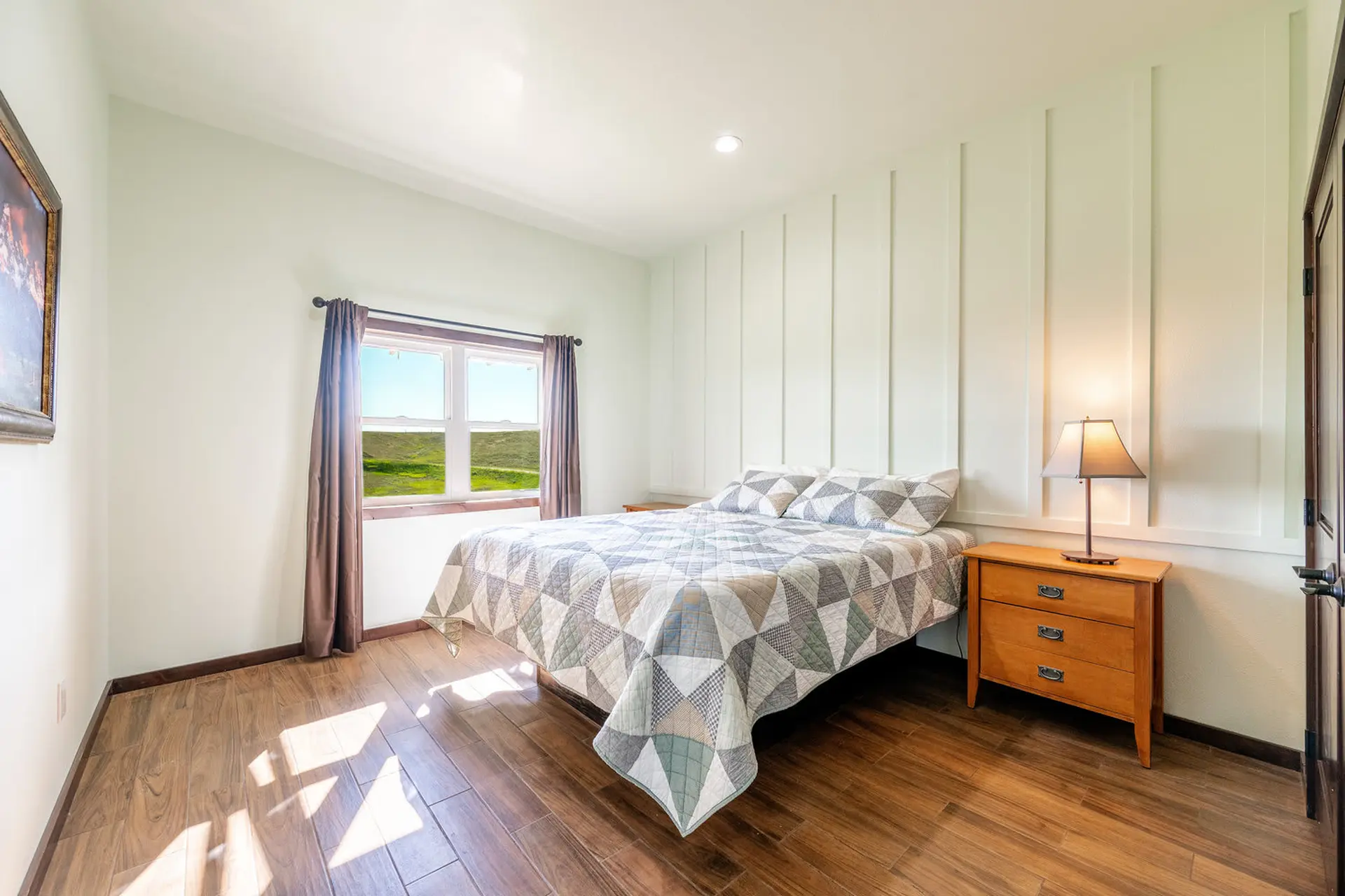 A bedroom with a bed, nightstand, and a window overlooking a green landscape.