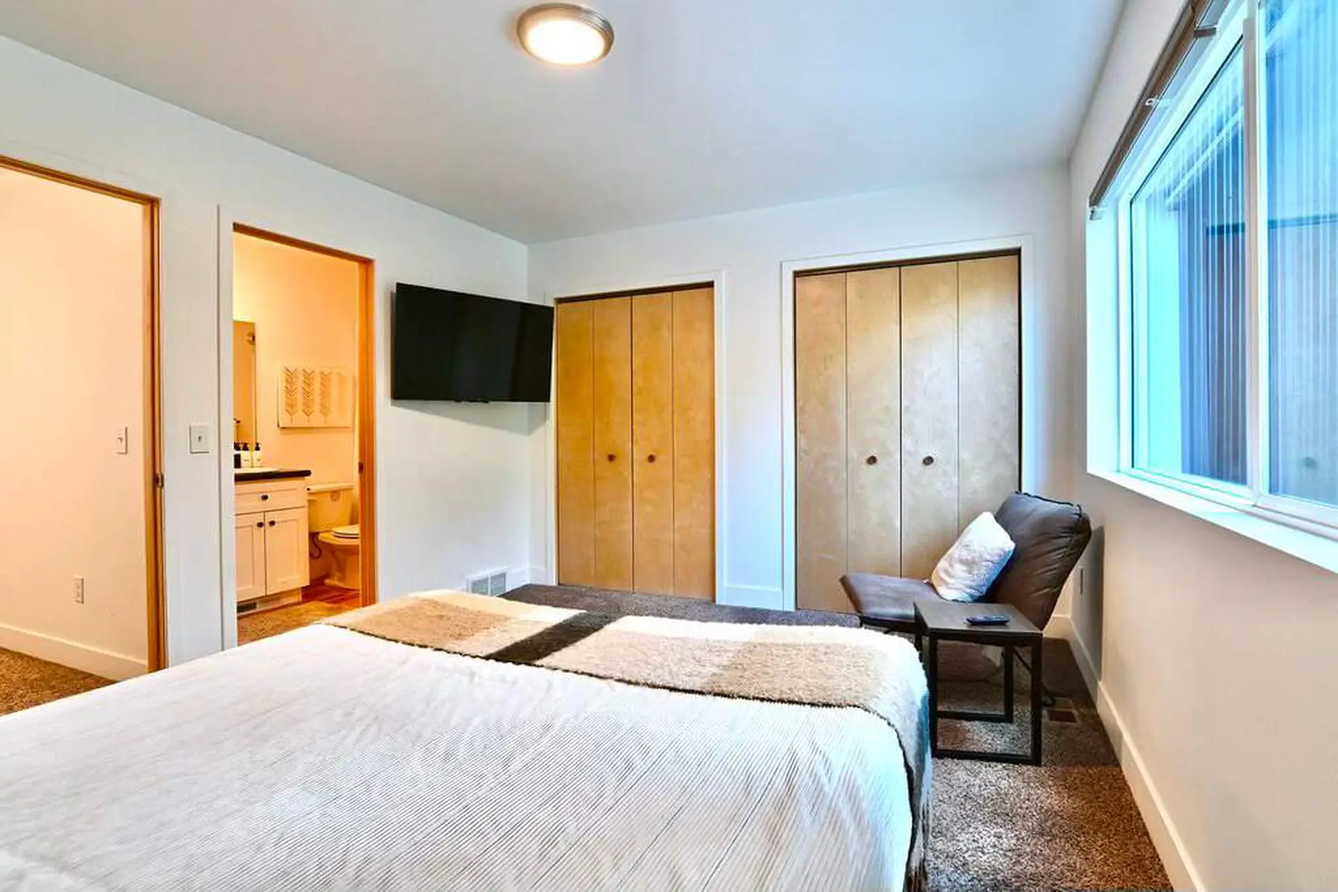 Bedroom with bed, TV, closet, chair, and a doorway to a bathroom.