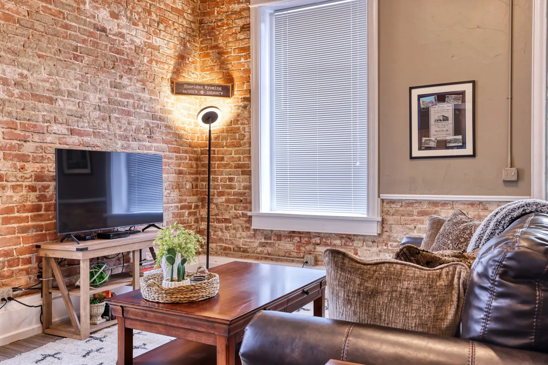 A living room with exposed brick, a TV, a coffee table, and a leather sofa.