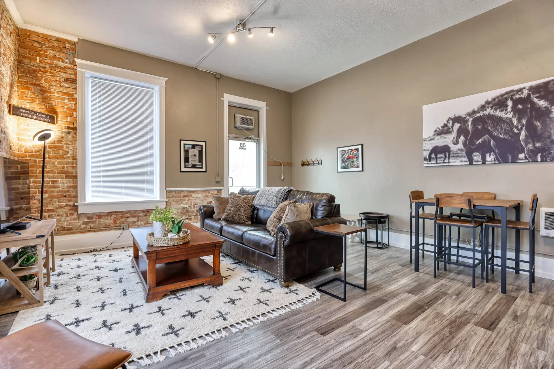 A living room with a brown leather couch, coffee table, and a high table with chairs.