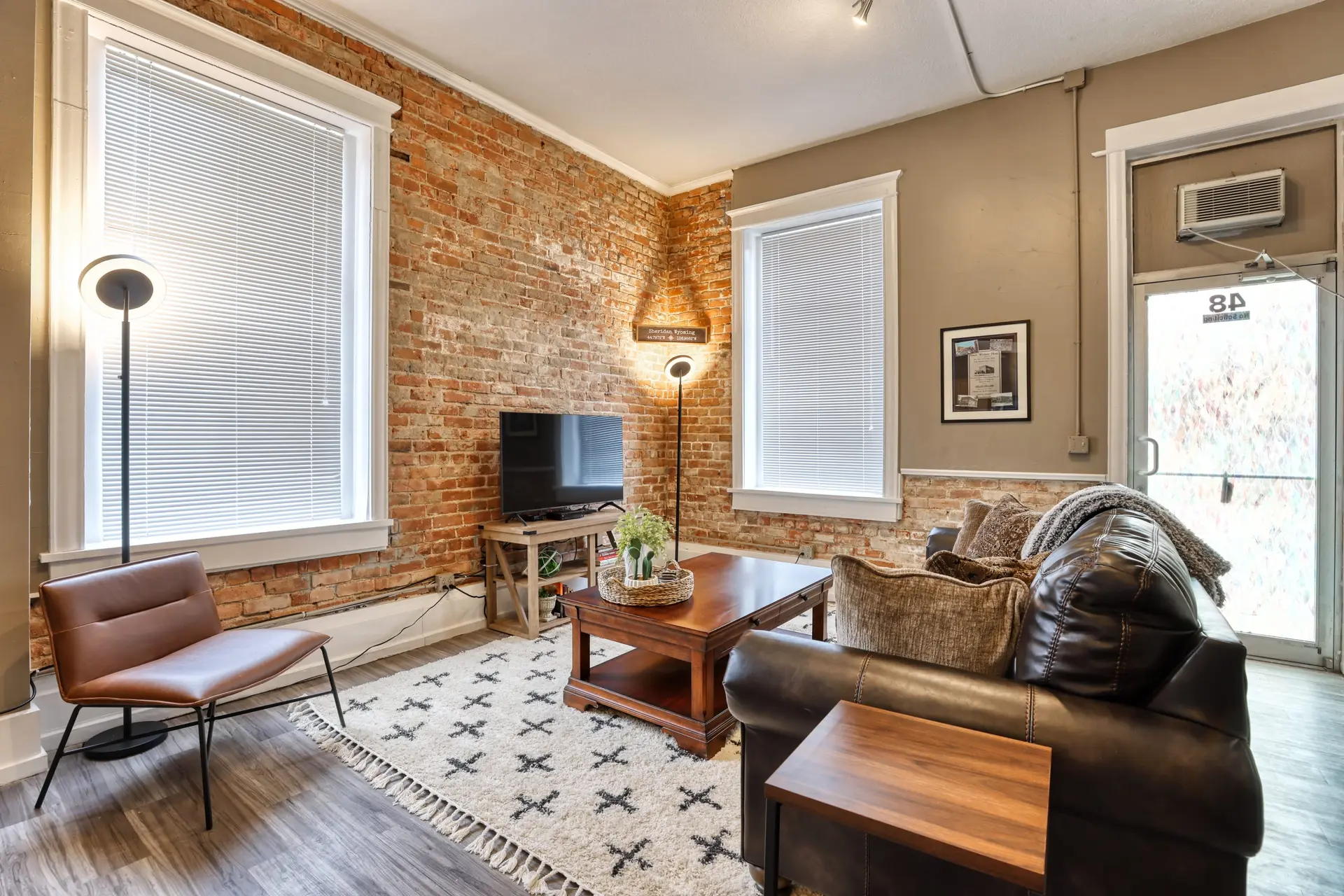 Living room with exposed brick, a brown leather sofa, and a floor lamp.