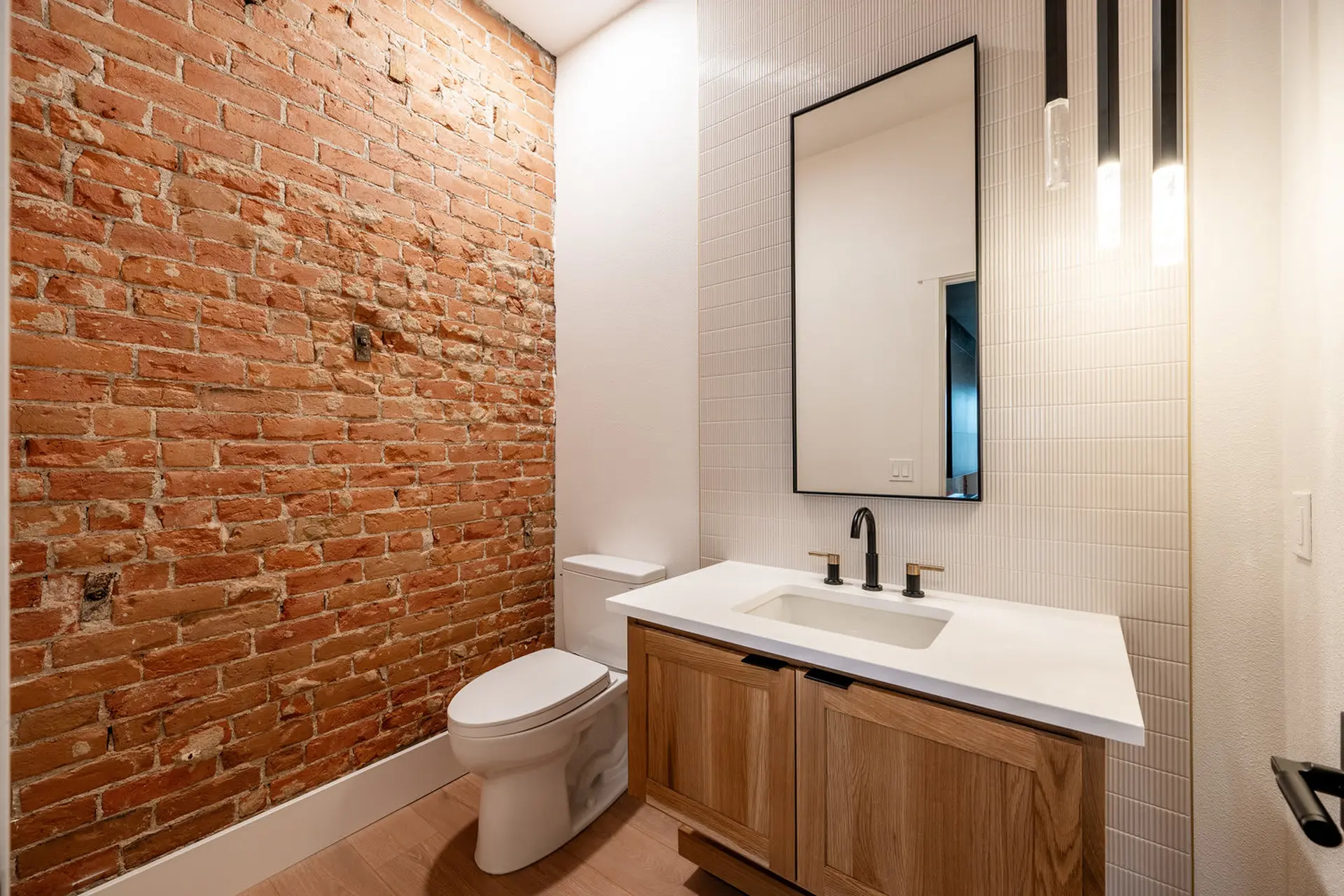 A modern bathroom with a brick accent wall, sleek vanity, and minimalist fixtures.