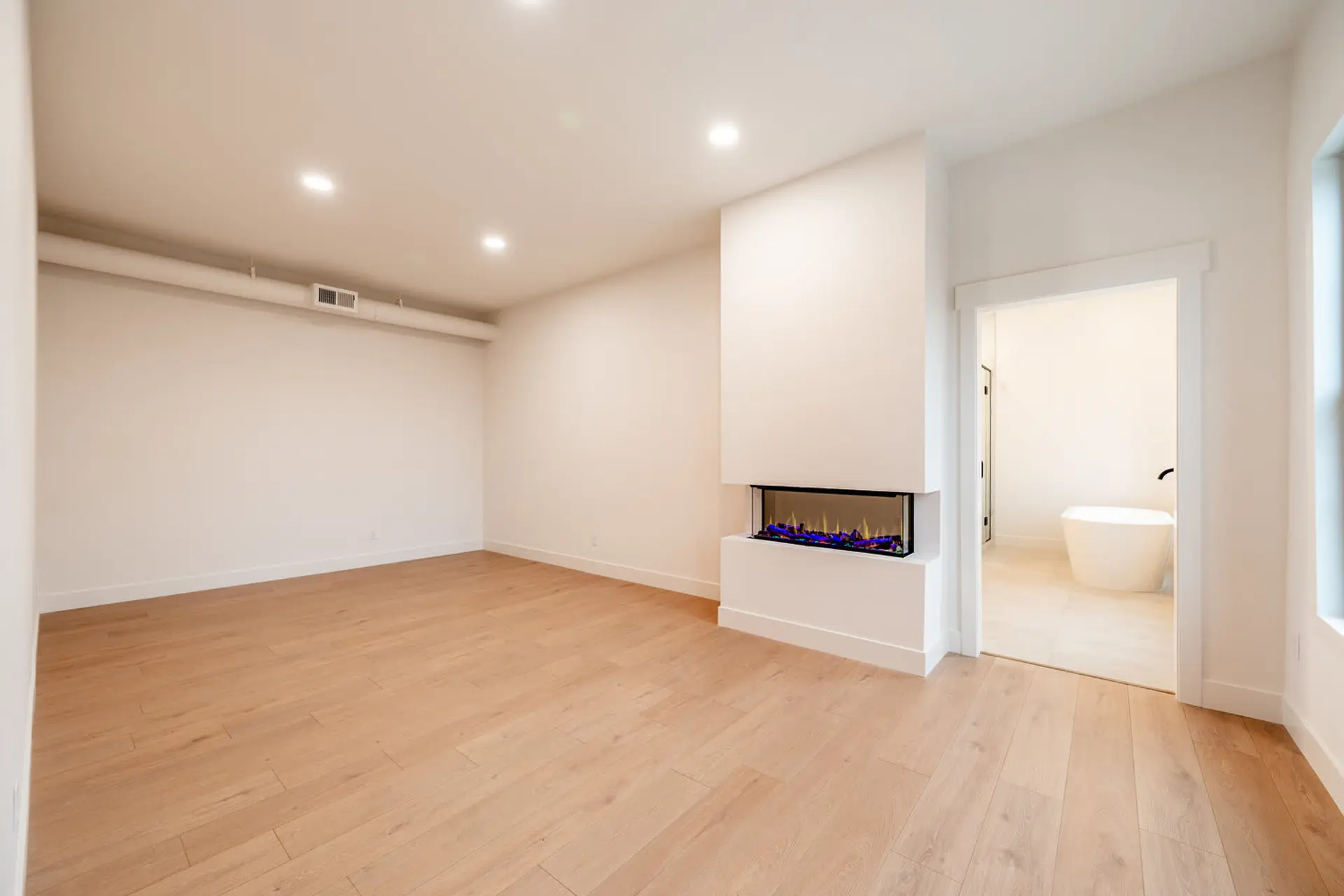 Modern living room with a corner fireplace and an adjacent bathroom with a freestanding tub.