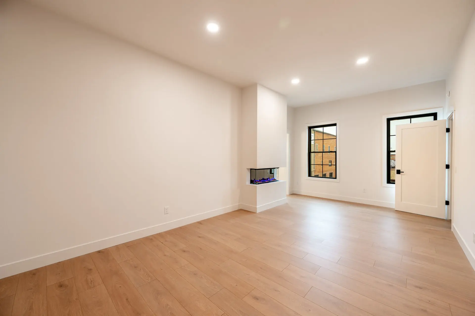 A bright, modern living room with light wood floors, white walls, and a fireplace.