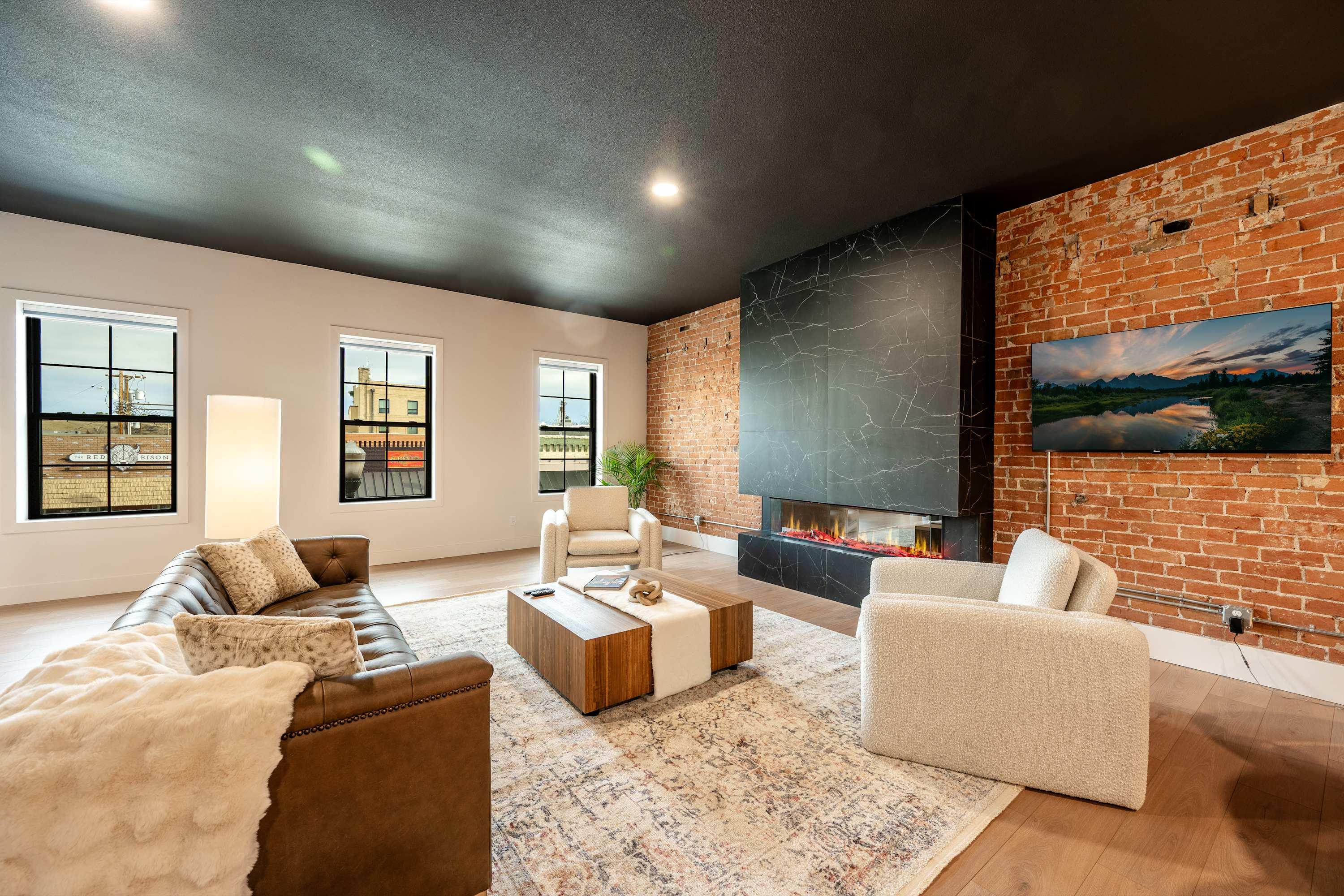 The Onyx living room at The Main Exchange set for a private gathering — exposed brick, linear fireplace, and steel-frame windows on Main Street.
